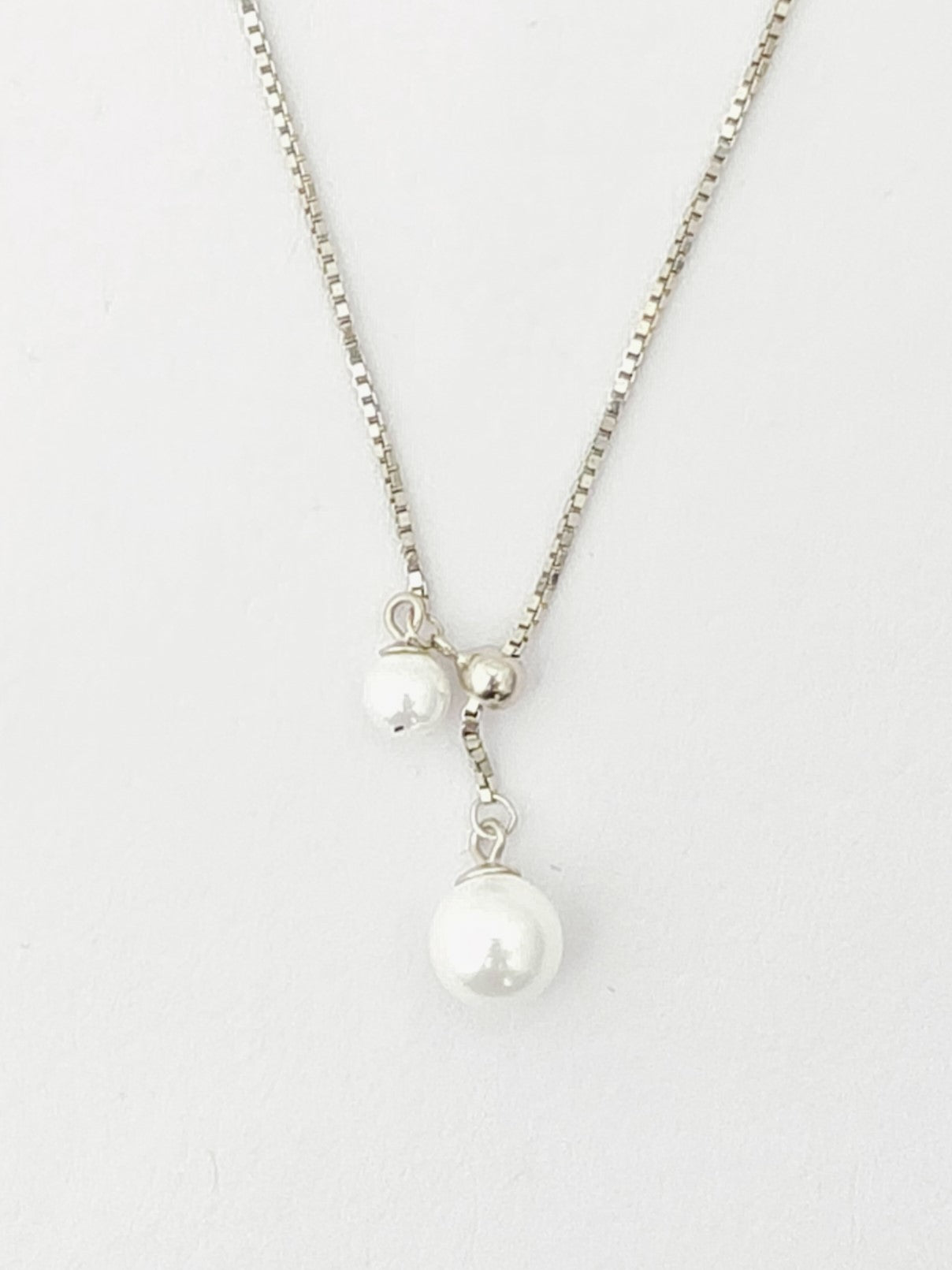 Pearl necklace with silver chain on a light gray background
