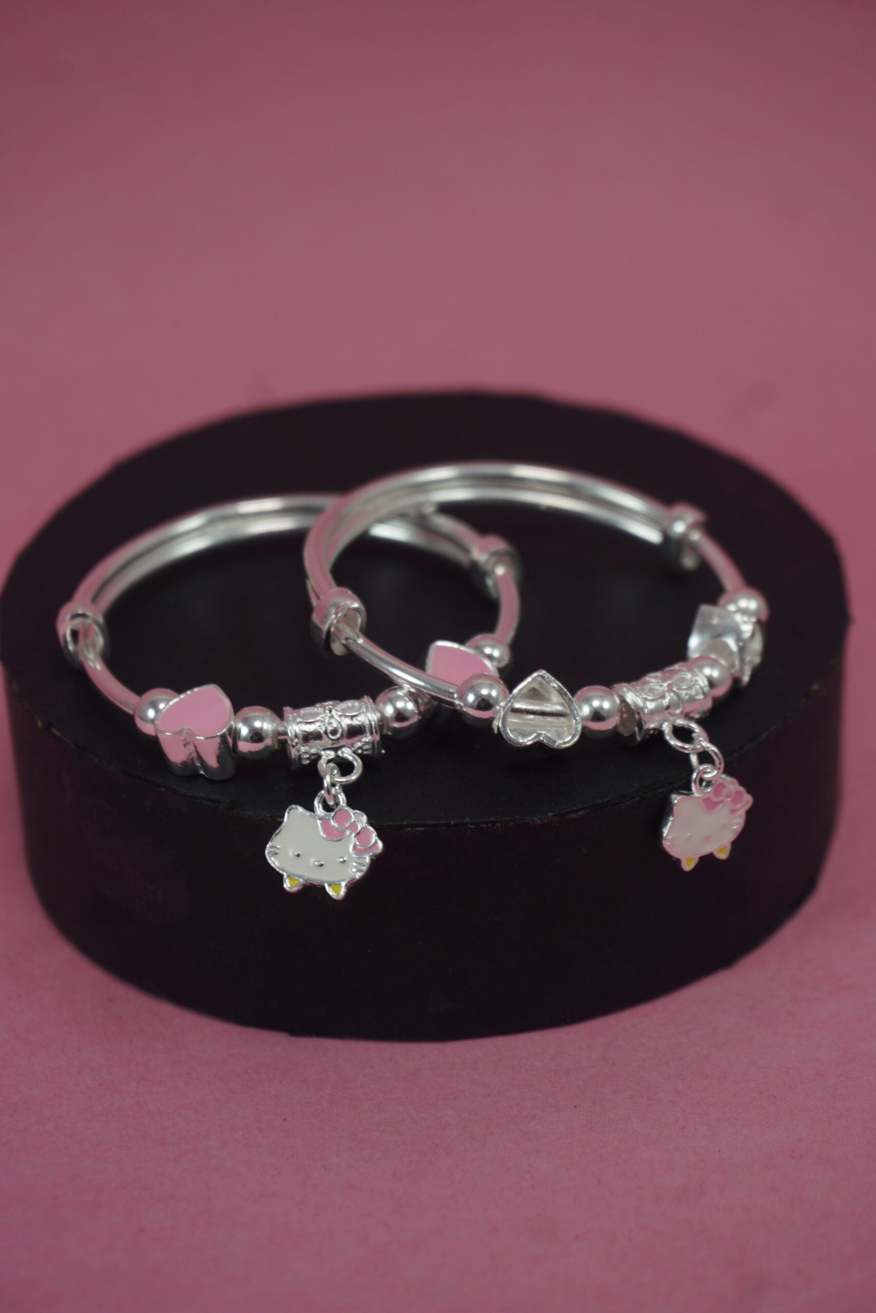 Silver hoop earrings with pink accents on a black stand against a pink background