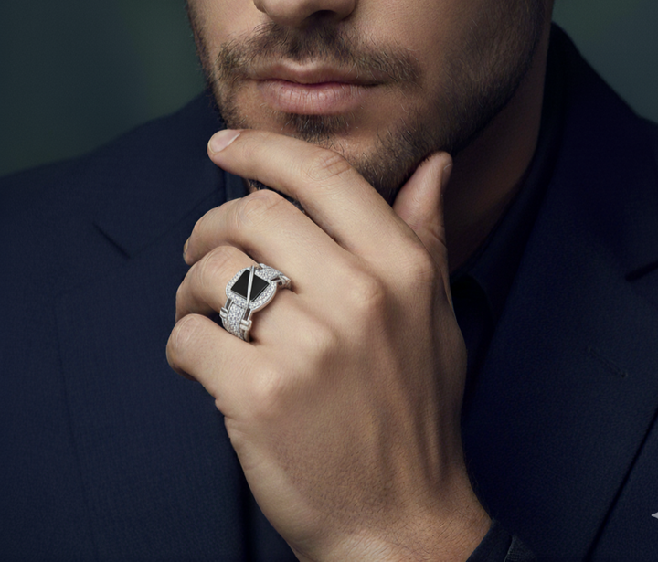 Man in a dark suit with a diamond ring on his finger against a dark background