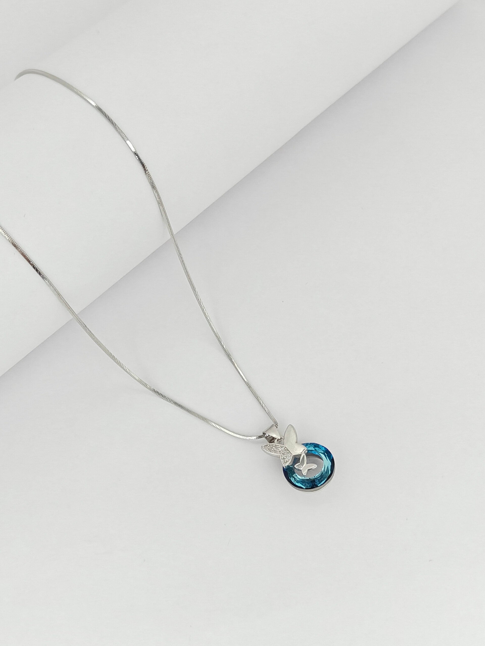 Silver necklace with a blue pendant on a light gray background