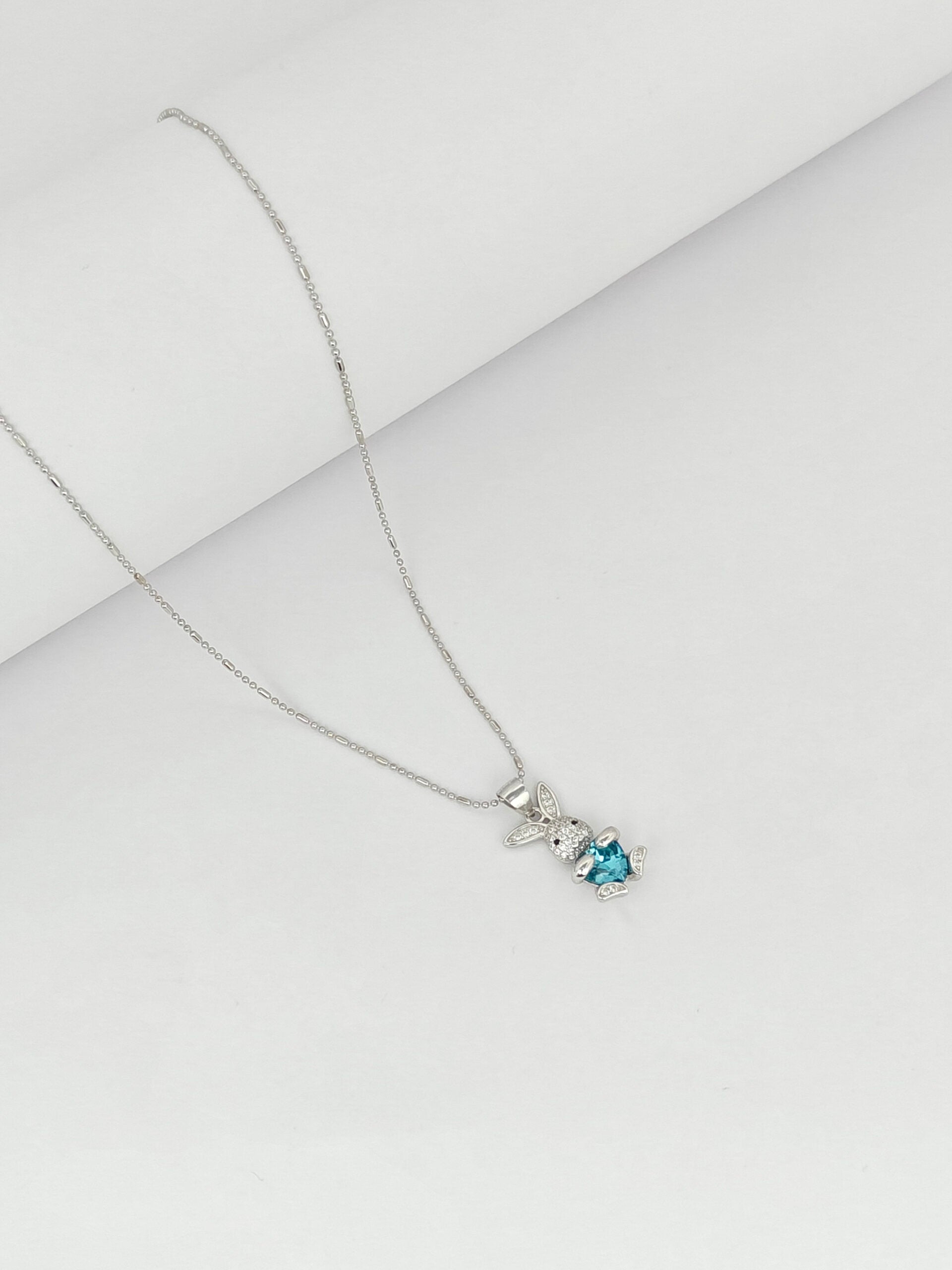 Silver necklace with a blue gemstone pendant on a light gray background