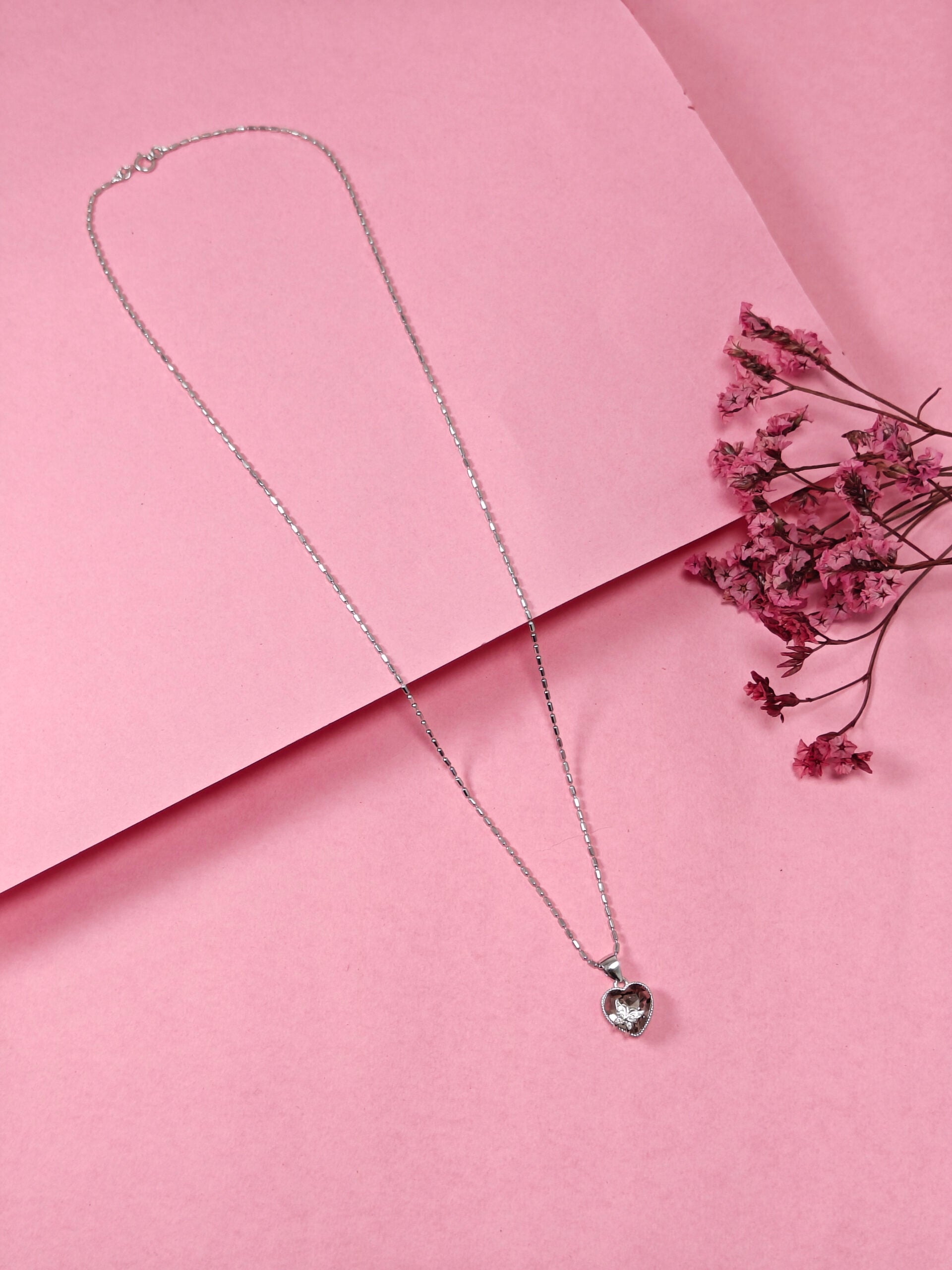 Silver necklace with a heart-shaped pendant on a pink background