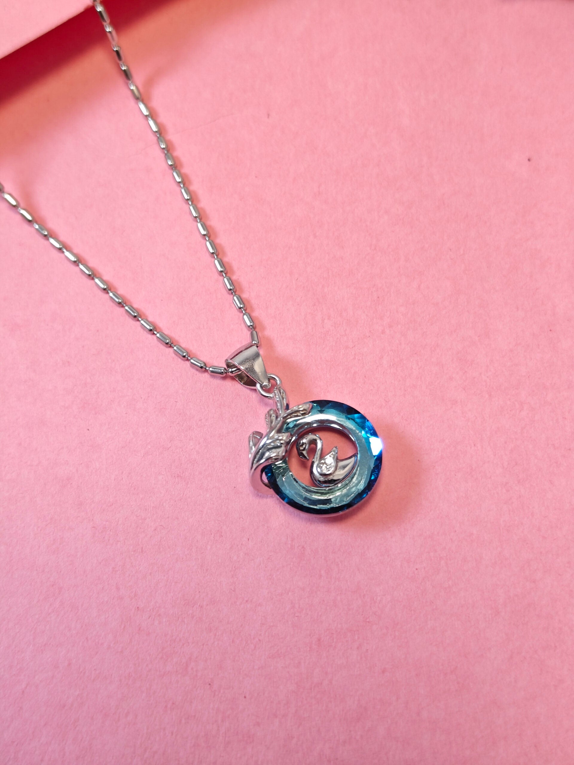 Silver necklace with a blue and silver pendant on a pink background