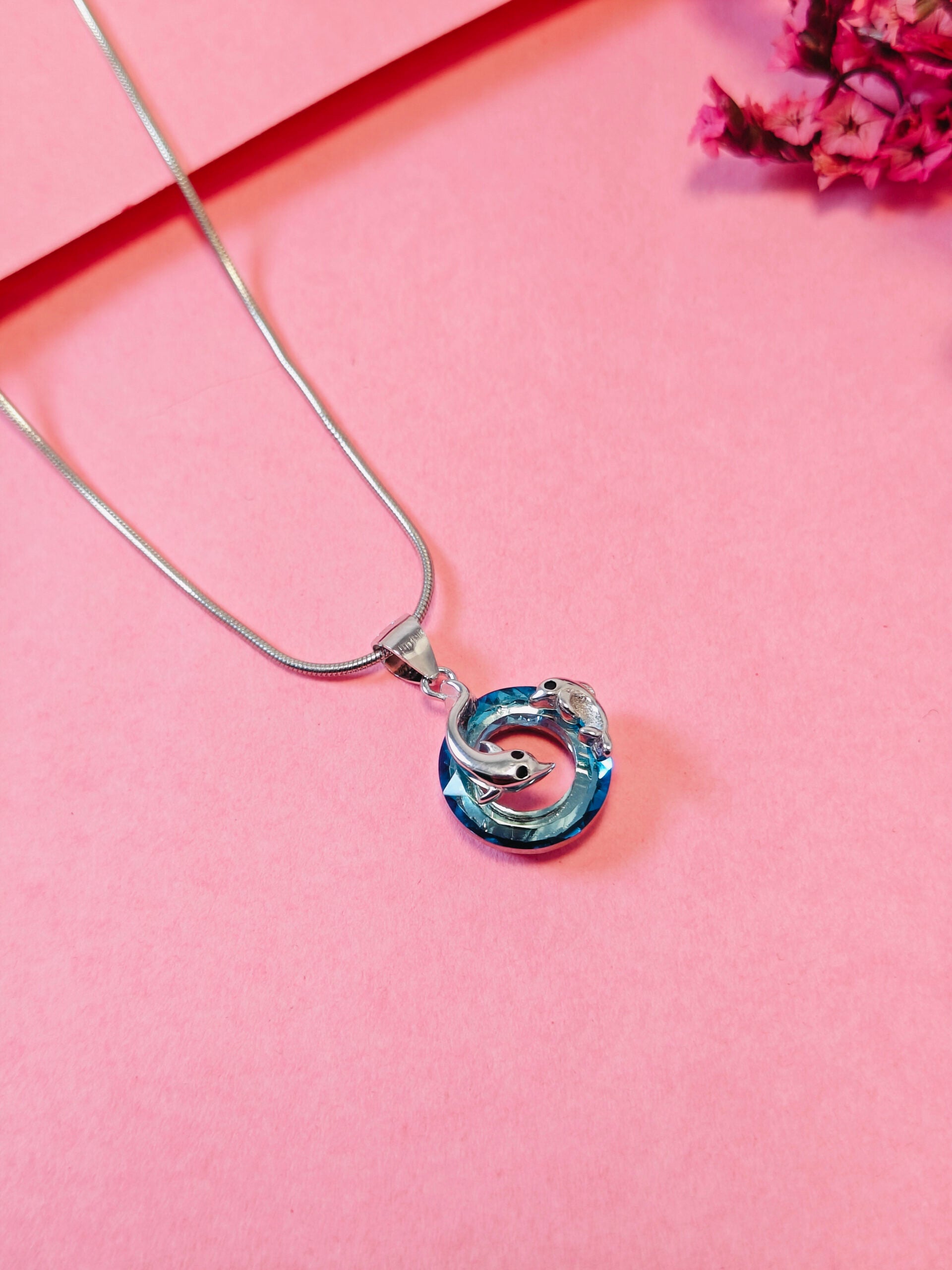 Necklace with a blue and silver pendant on a pink background