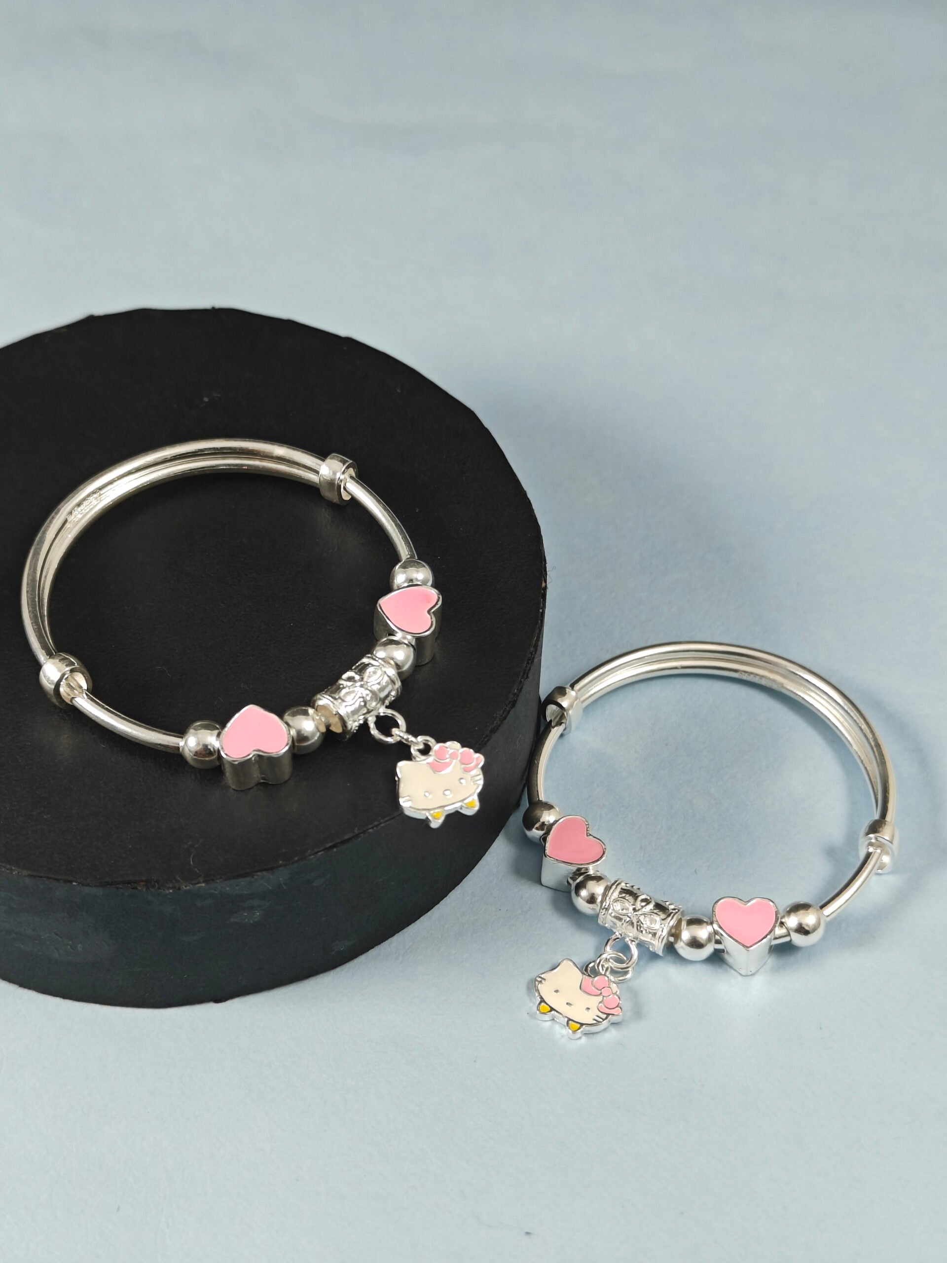Silver bracelets with pink heart charms on a gray background