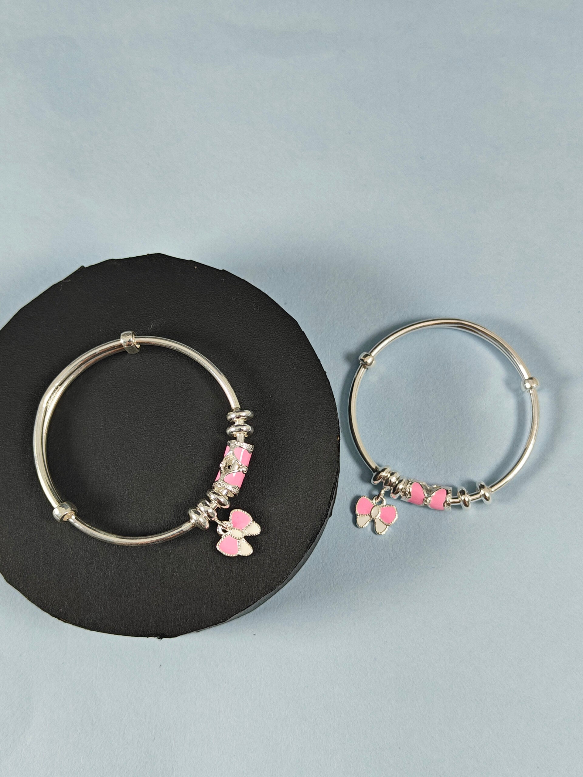 Silver hoop earrings with pink heart charms on a black stand against a light blue background
