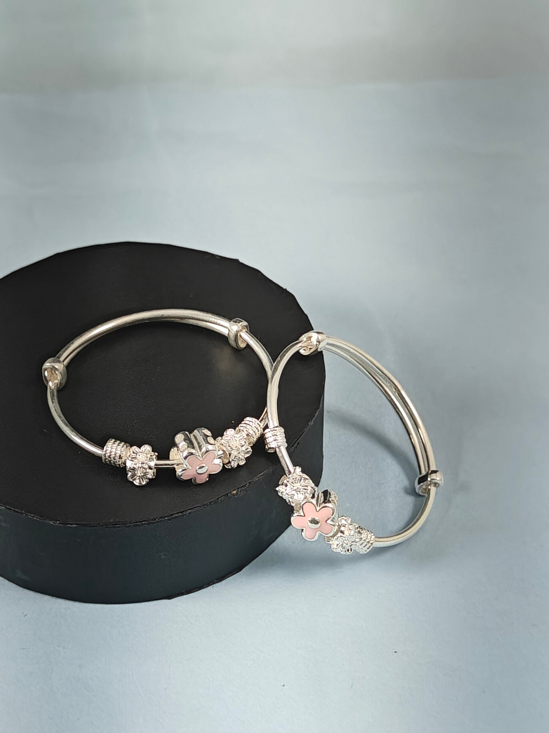 Silver bangles with floral charms on a gray background