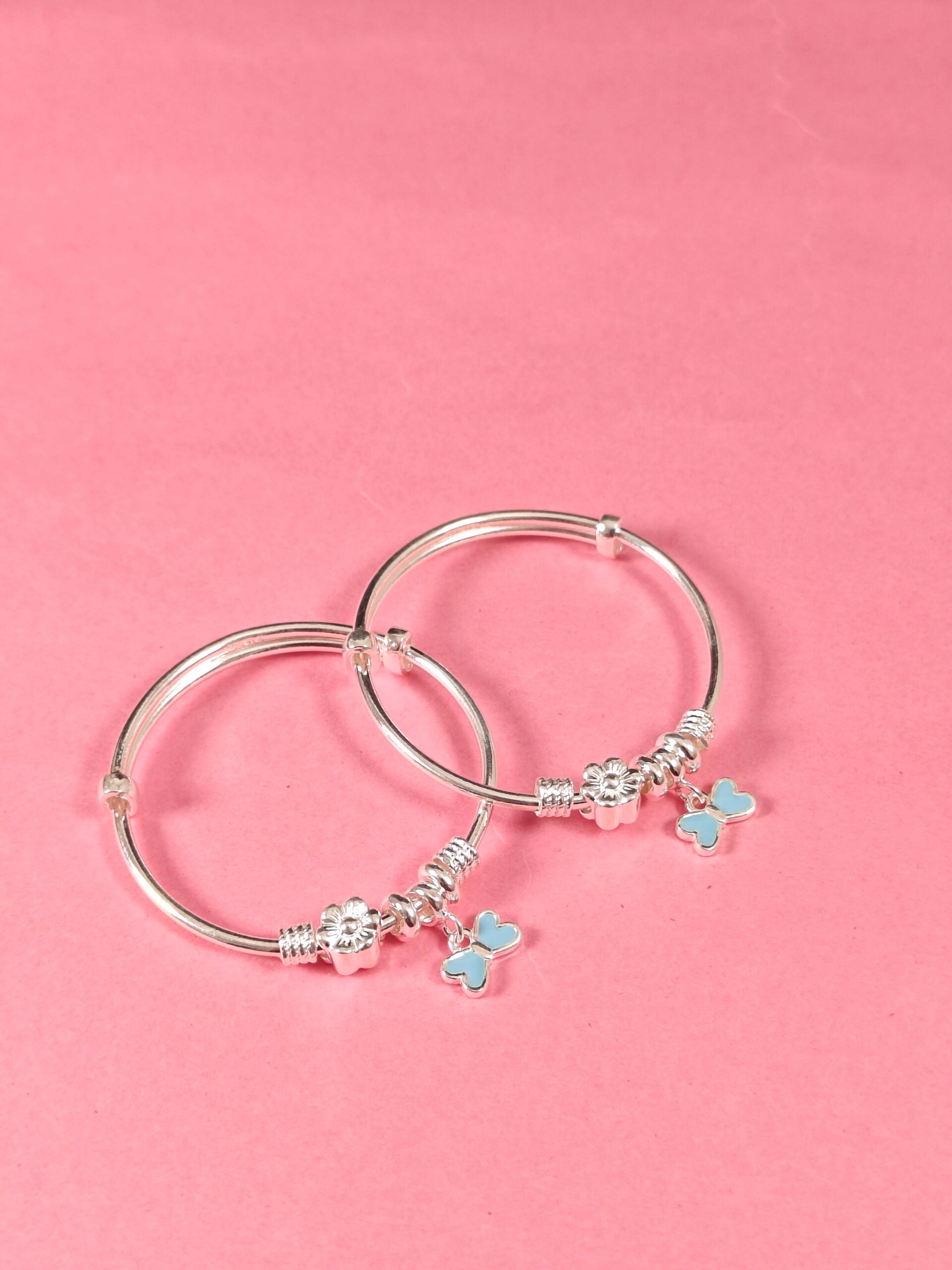 Silver bangles with butterfly charms on a pink background