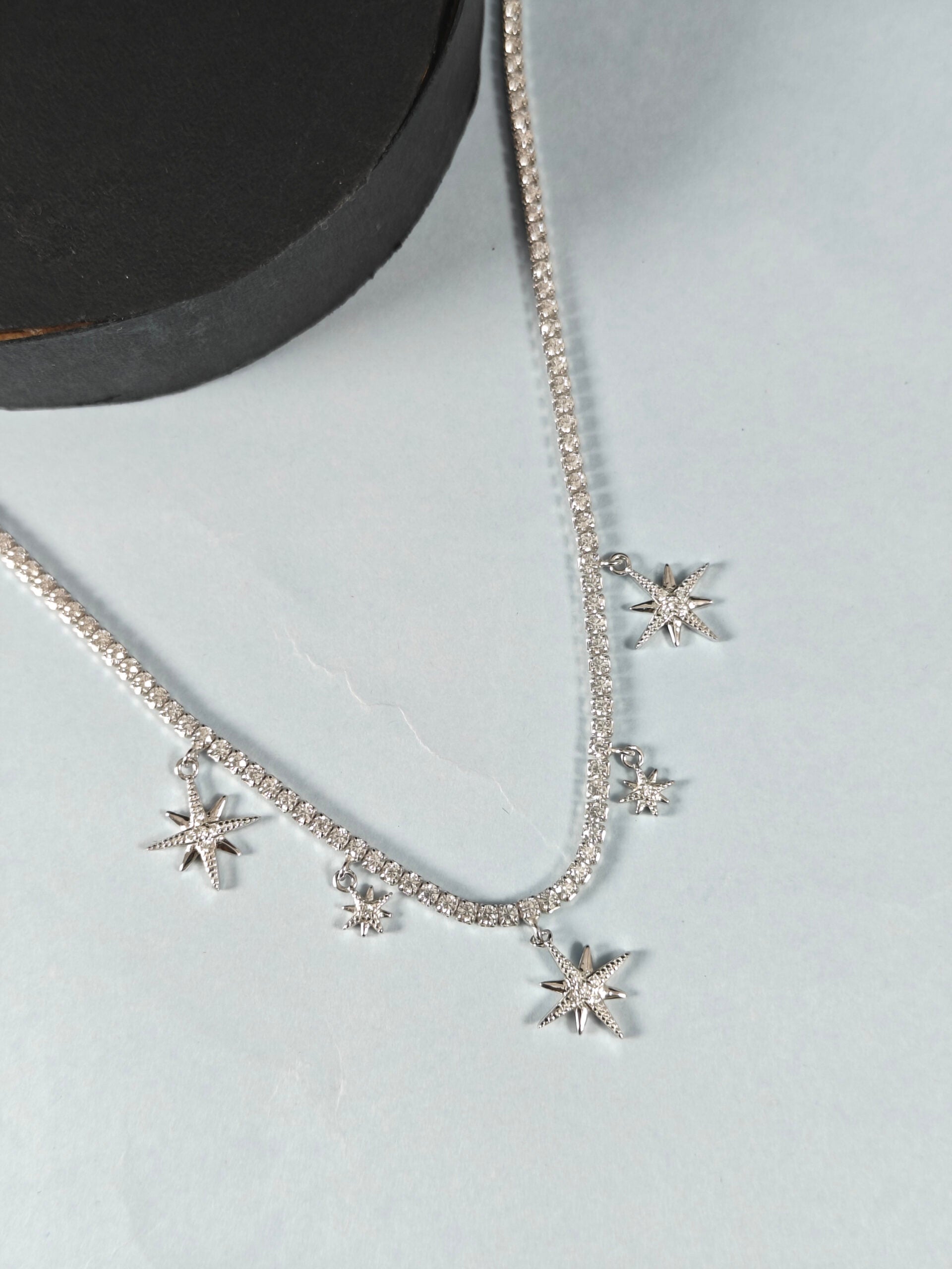 Silver necklace with star-shaped pendants on a light gray background