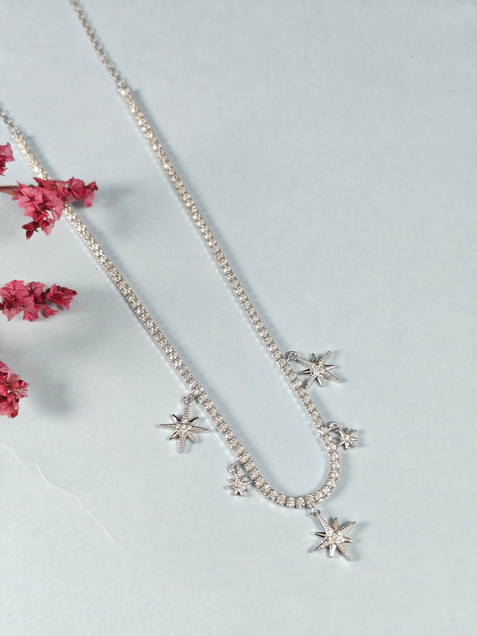 Silver necklace with star-shaped pendants on a light gray background