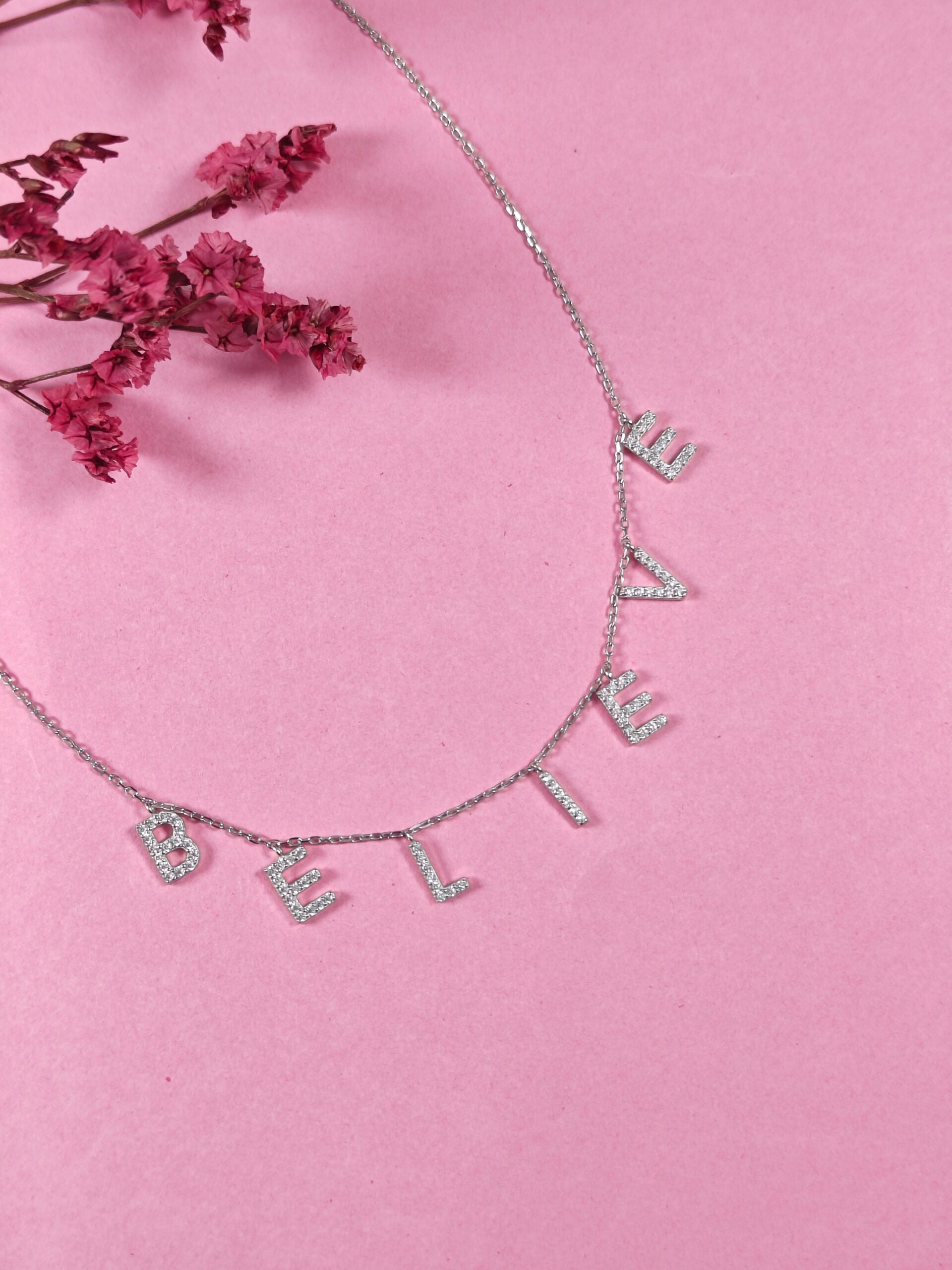 Necklace with 'BELIEVE' letters on a pink background