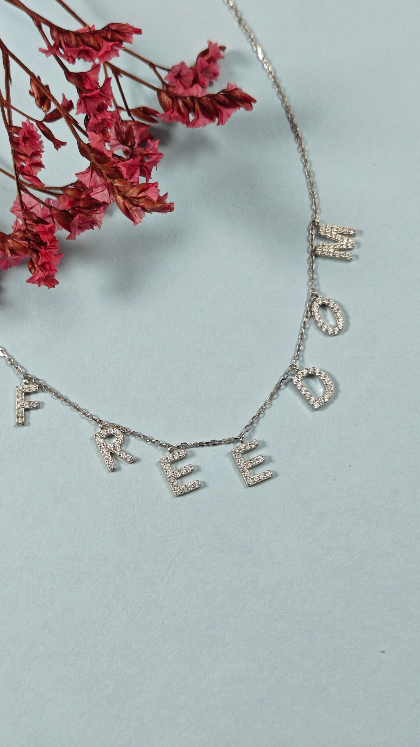Necklace with 'FREEDOM' pendant on a light gray background