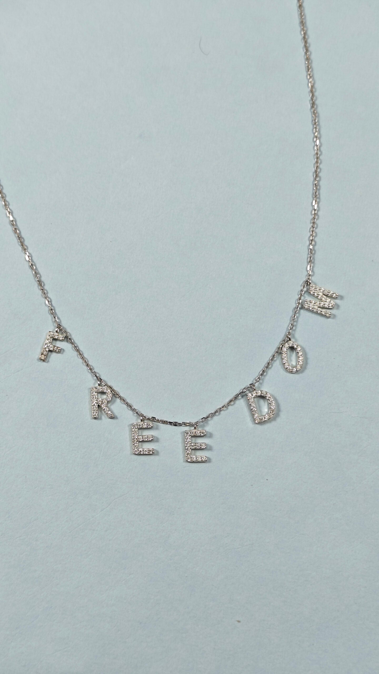 Necklace with diamond-studded letters spelling 'FREEDOM' on a light gray background