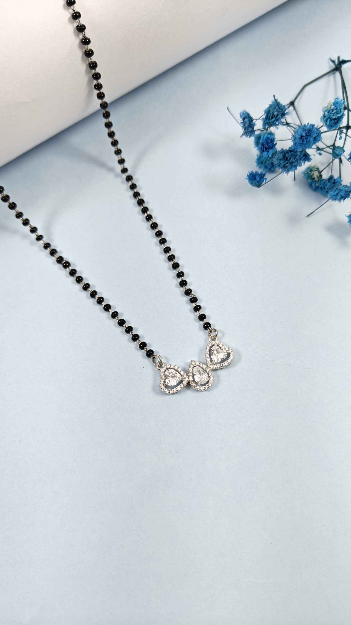 Necklace with black beads and a silver pendant on a light blue background