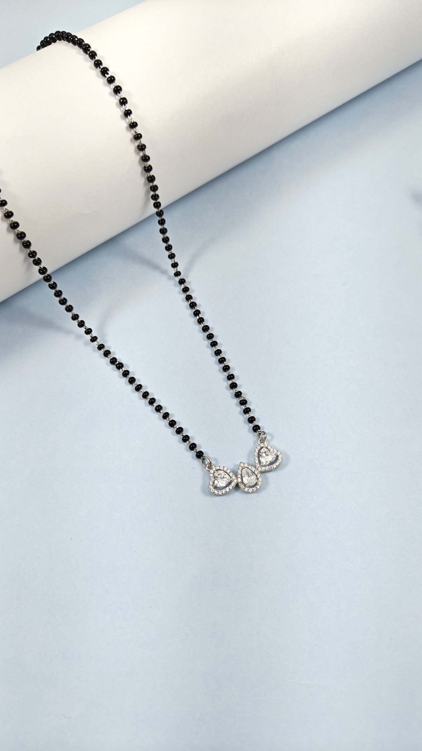 Necklace with black beads and silver heart pendants on a light blue background