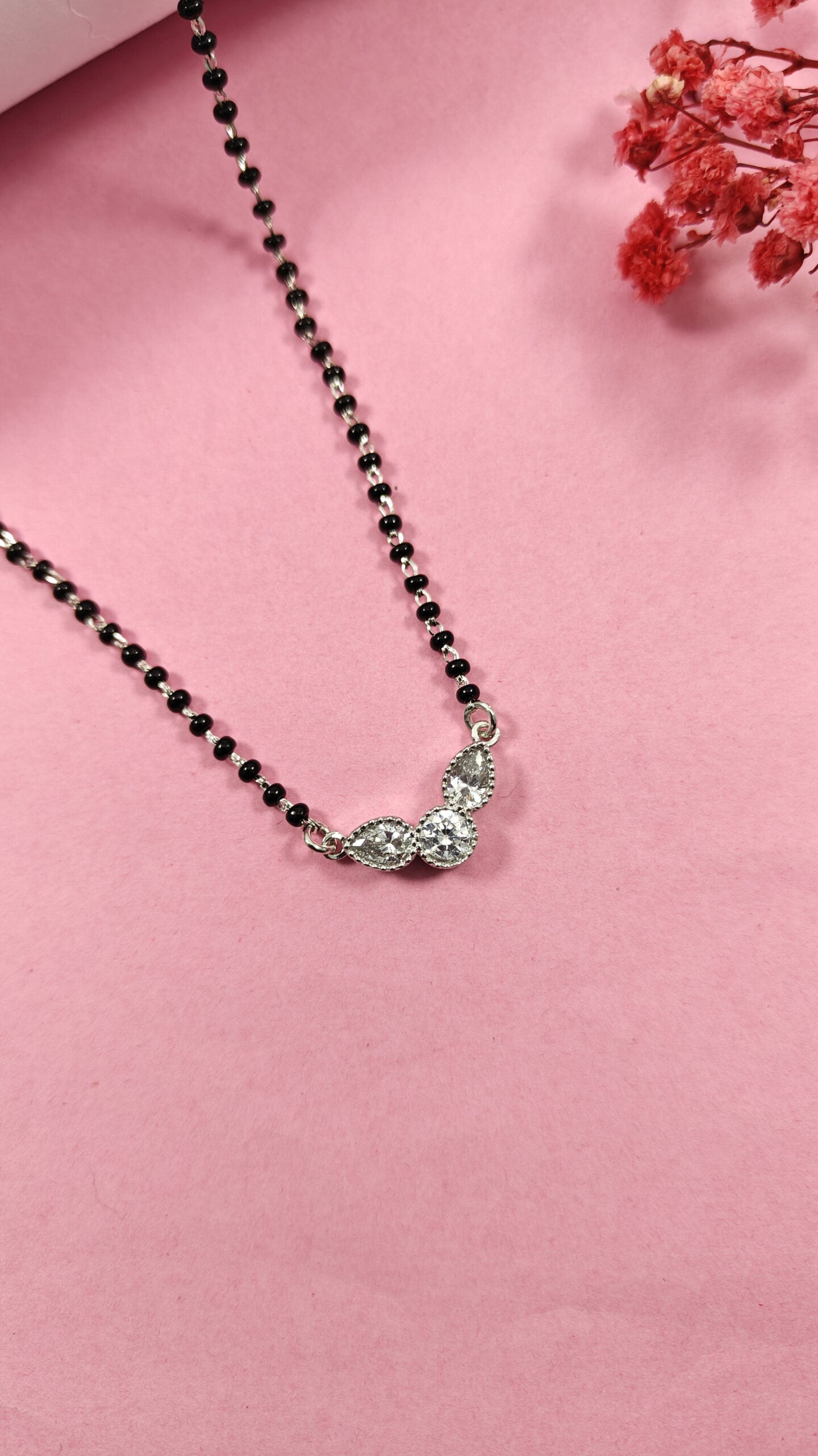 Necklace with black beads and a silver pendant on a pink background