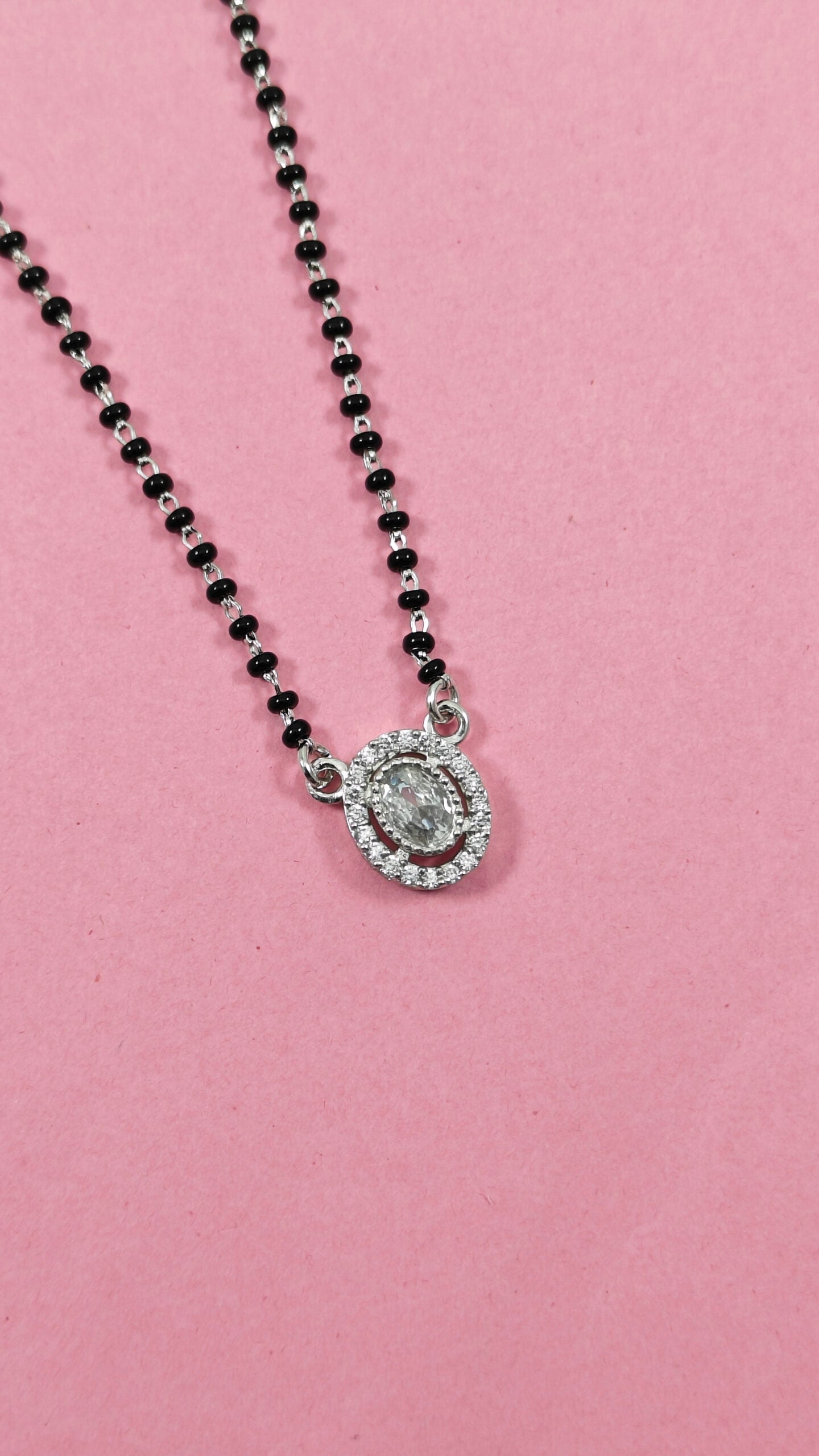 Necklace with black beads and a silver pendant on a pink background
