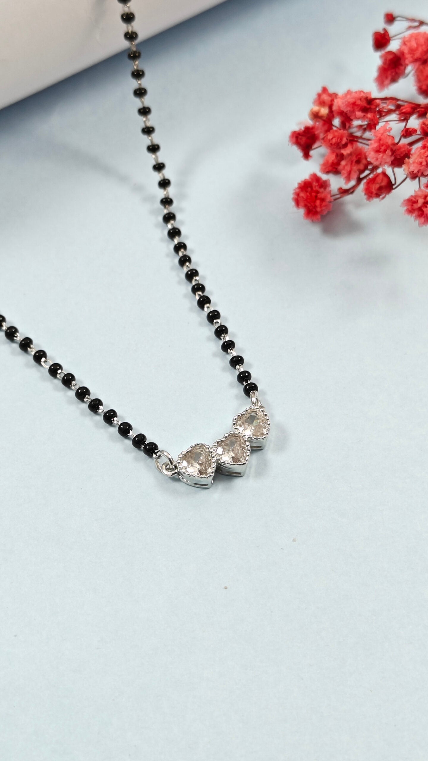 Necklace with black beads and silver pendants on a light gray background