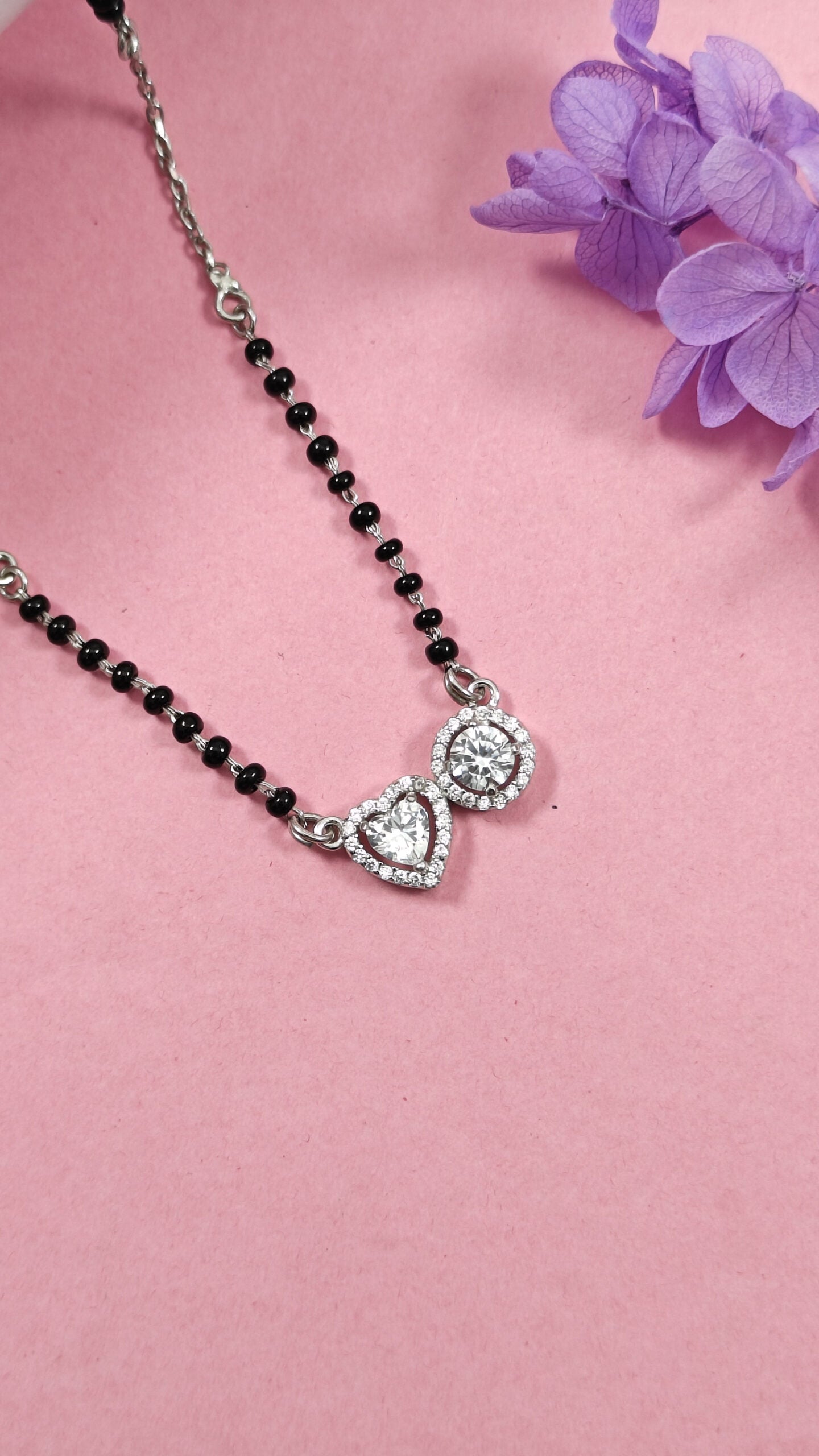 Necklace with a heart-shaped pendant on a pink background with purple flowers