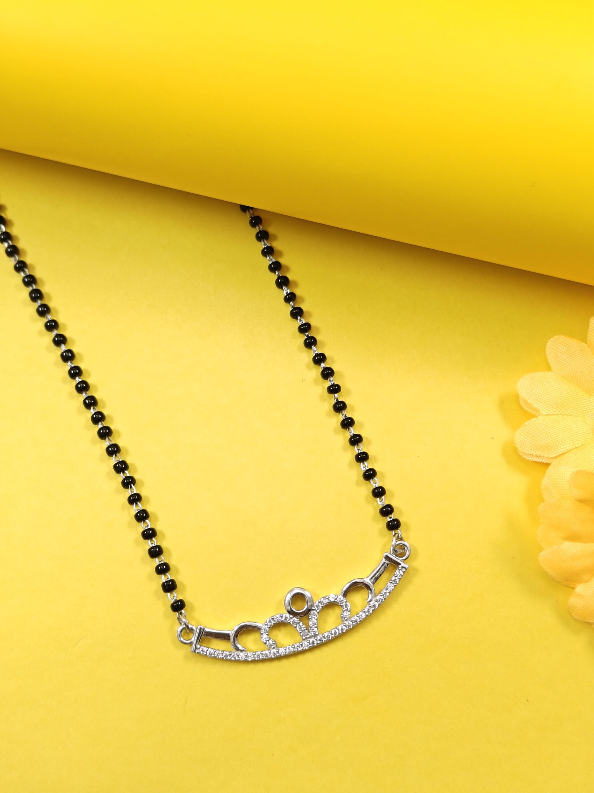 Black beaded necklace with a silver clasp on a yellow background