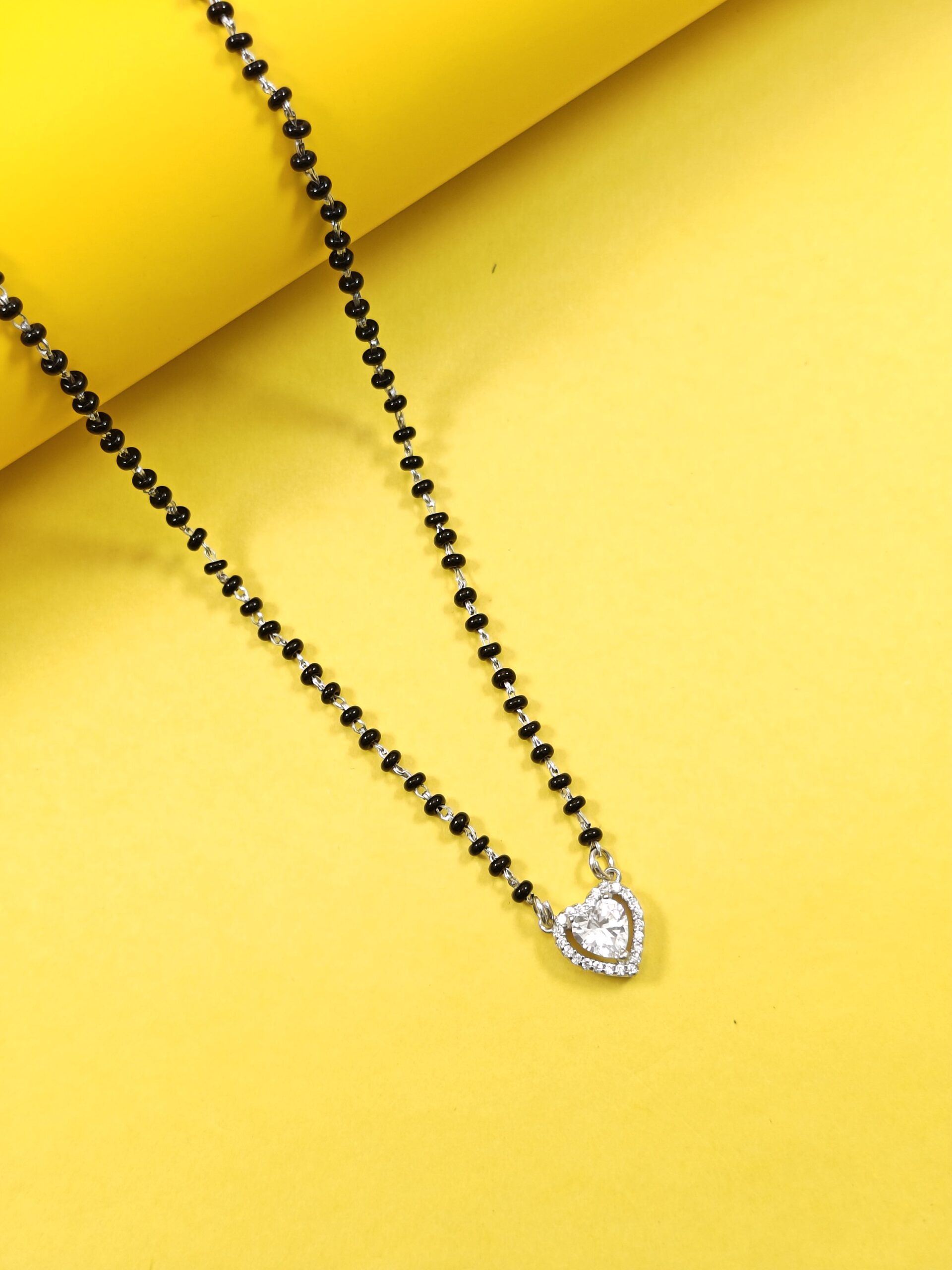 Black beaded necklace with a heart-shaped silver pendant on a yellow background