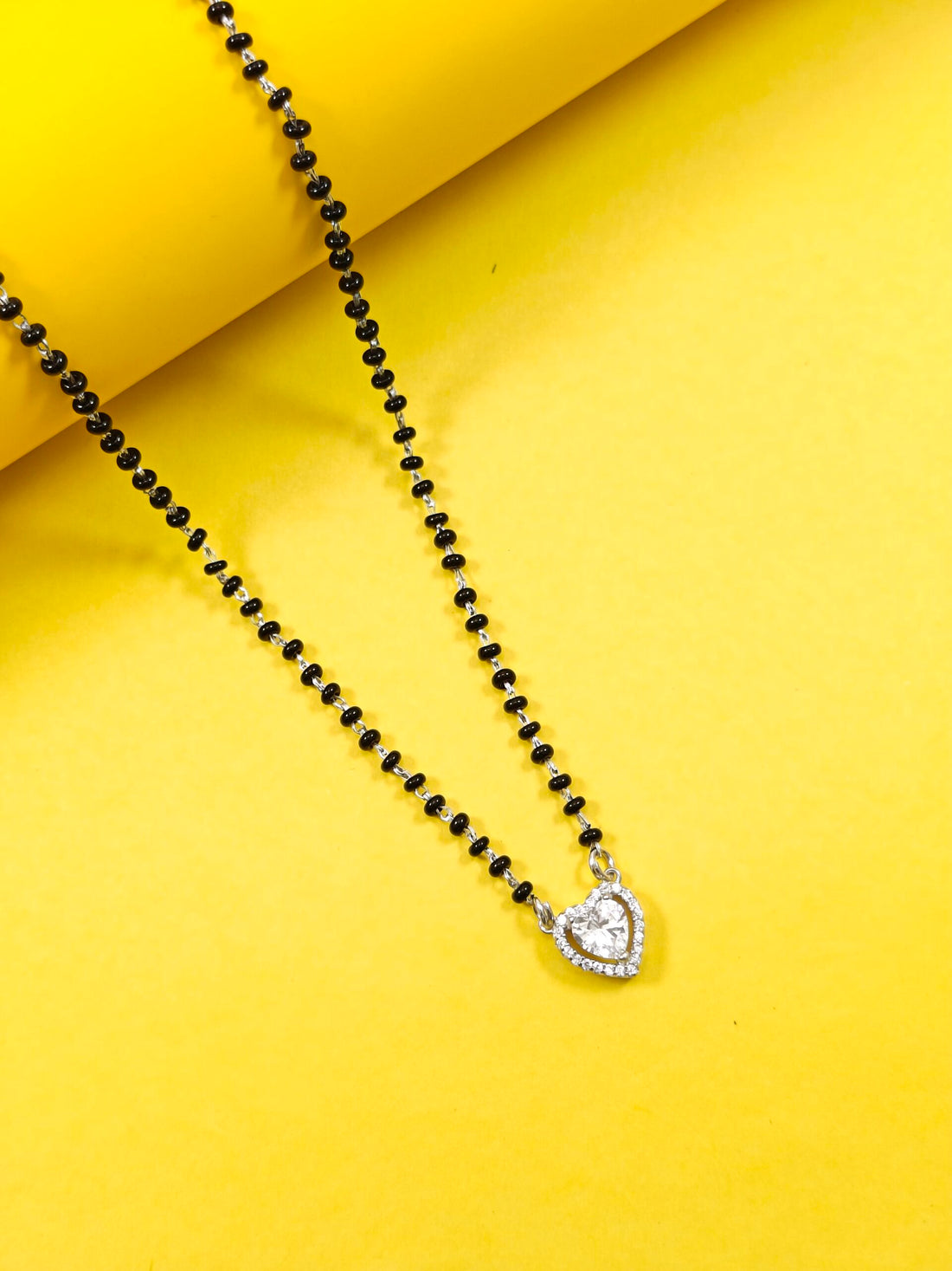 Black beaded necklace with a heart-shaped silver pendant on a yellow background