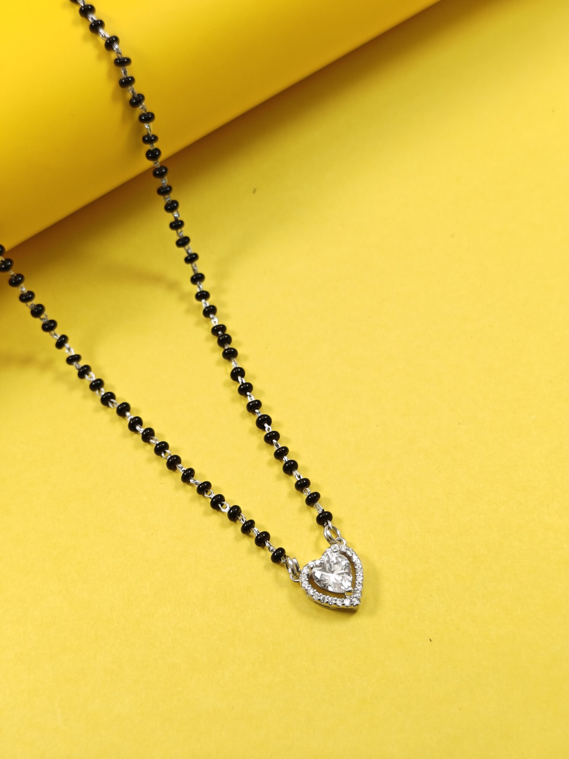 Black beaded necklace with a silver pendant on a yellow background