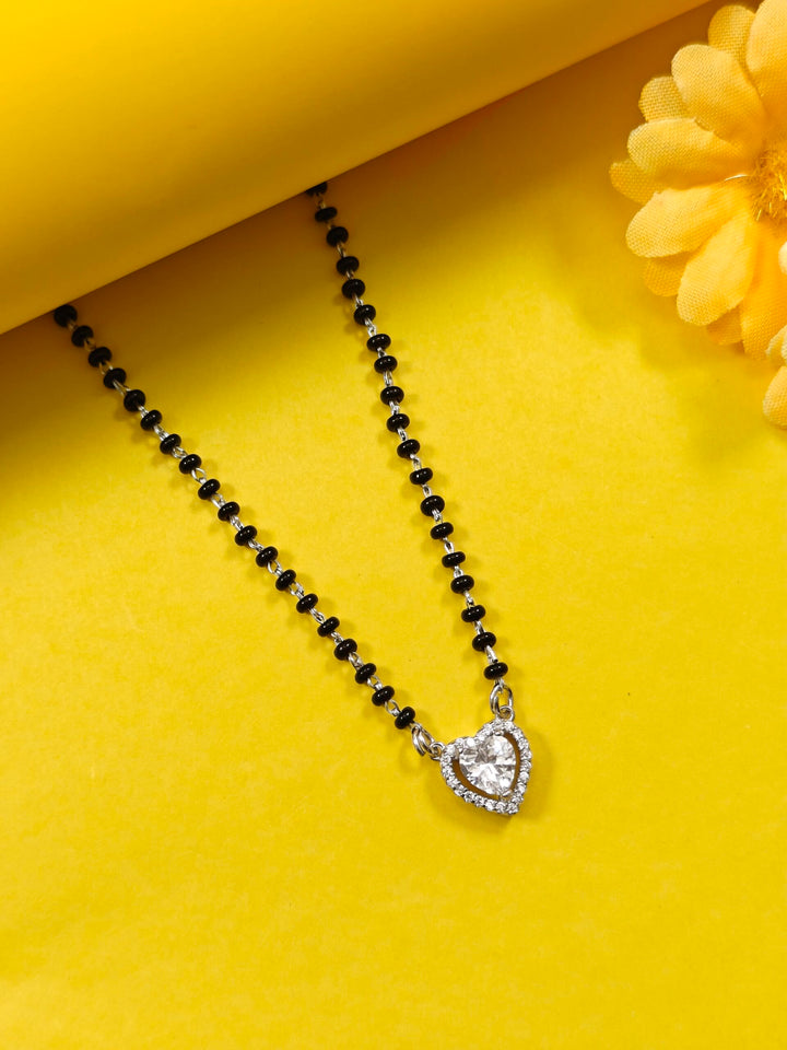 Black beaded necklace with a heart-shaped silver pendant on a yellow background