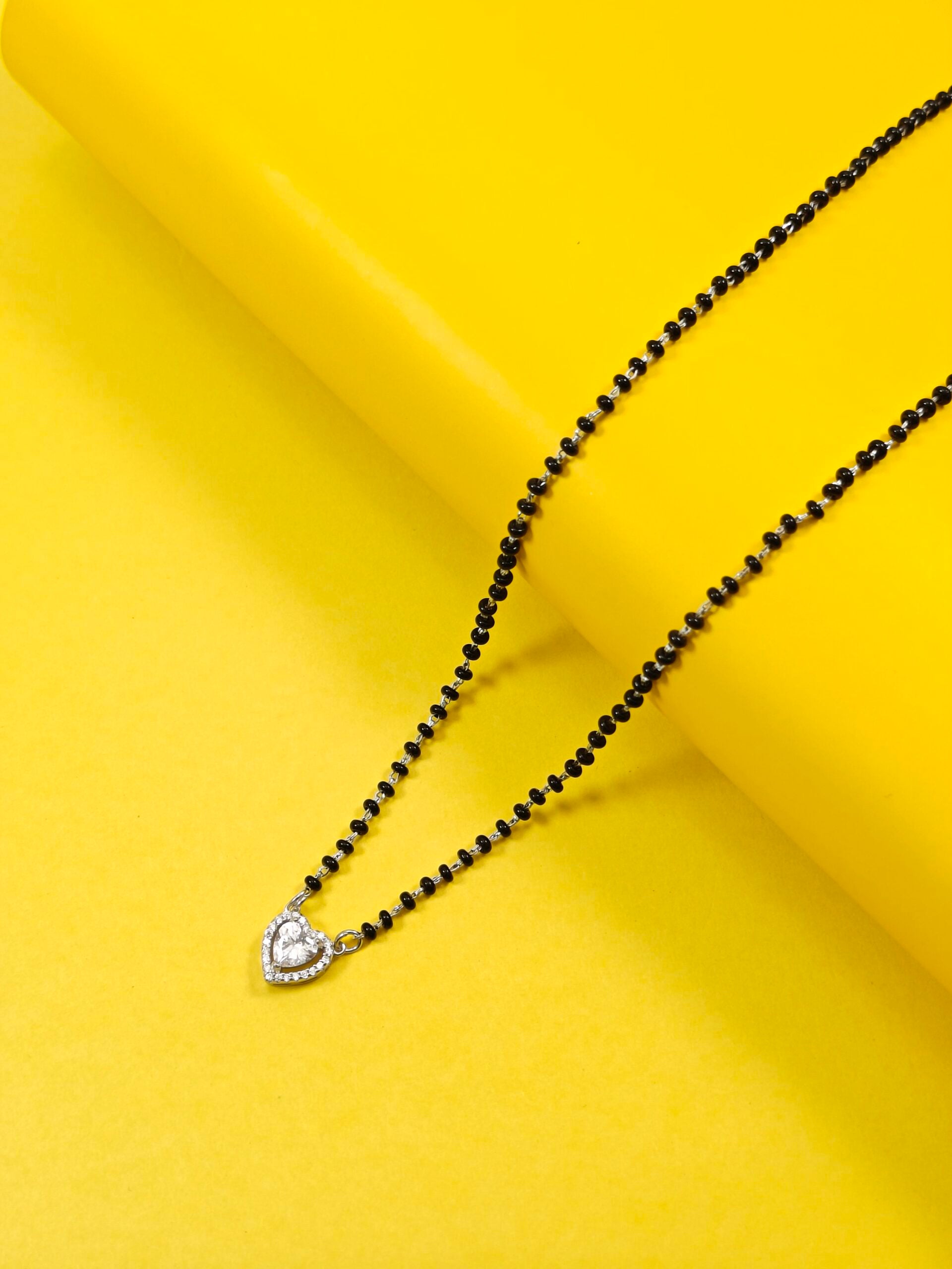 Black beaded necklace with a heart-shaped pendant on a yellow background