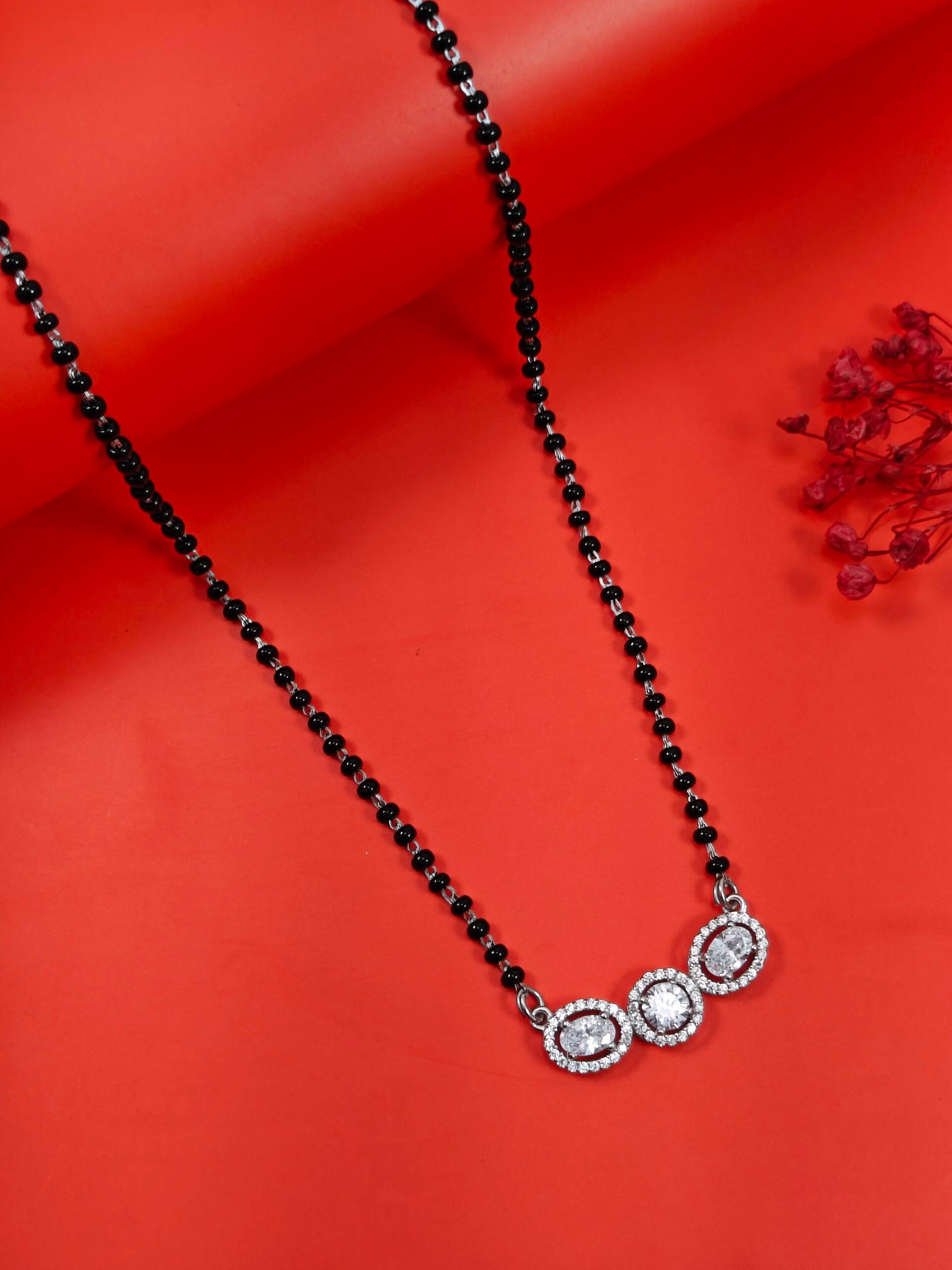 Black beaded necklace with a silver and crystal pendant on an orange background