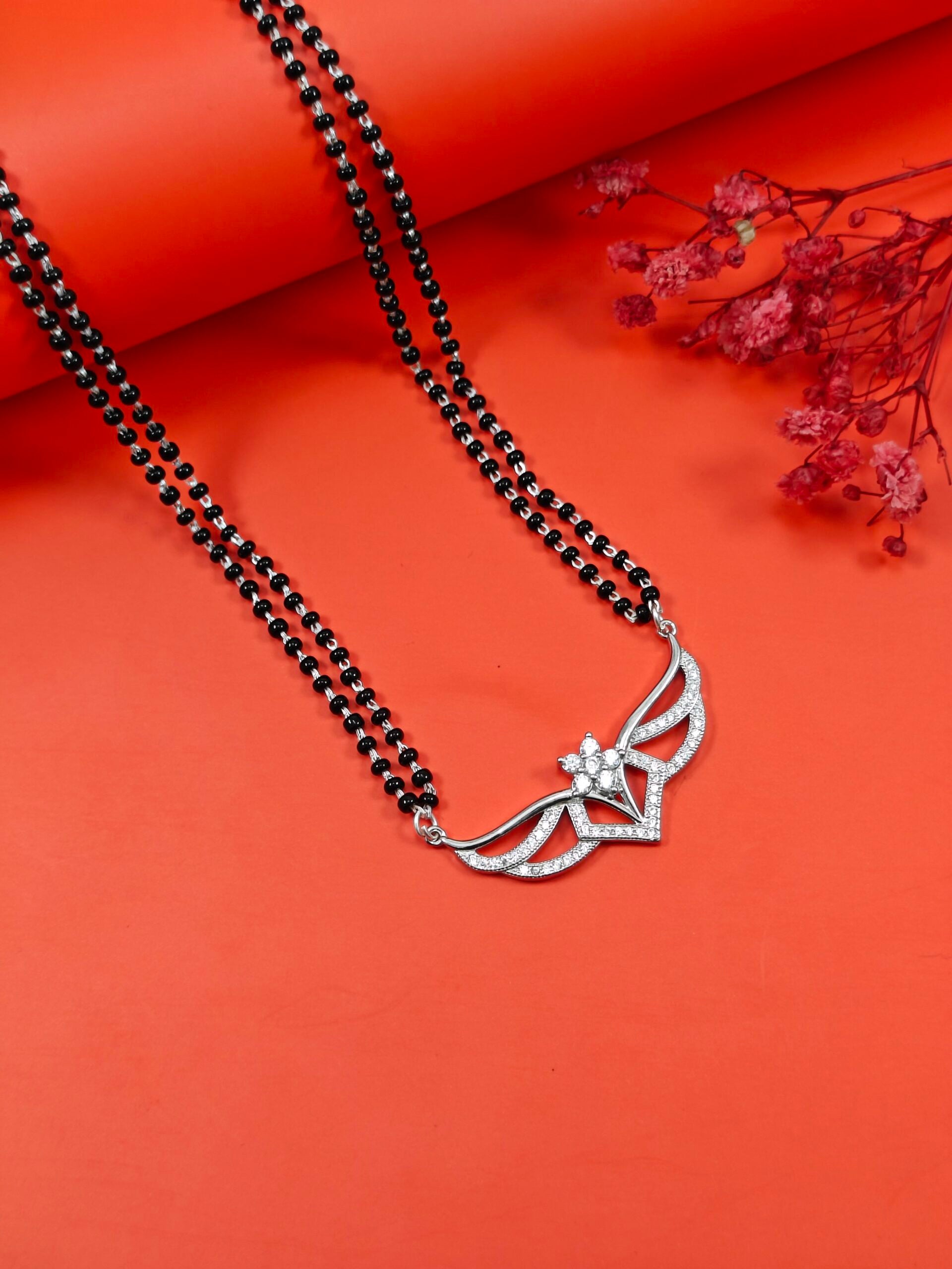 Black beaded necklace with a silver floral pendant on an orange background