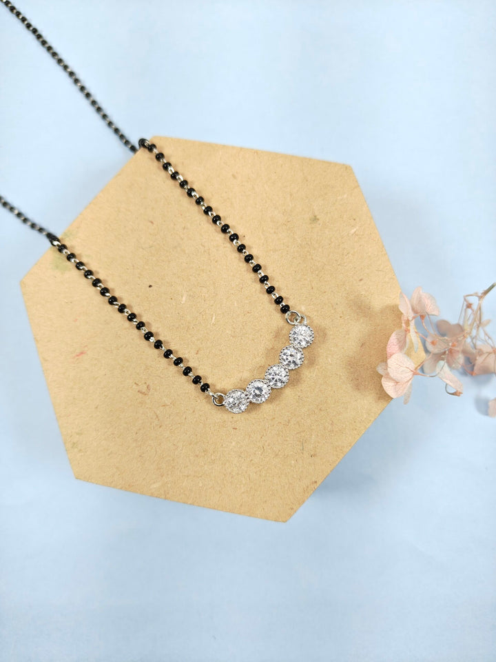 Necklace with black beaded chain and silver clasp on a hexagonal cardboard stand against a light blue background.