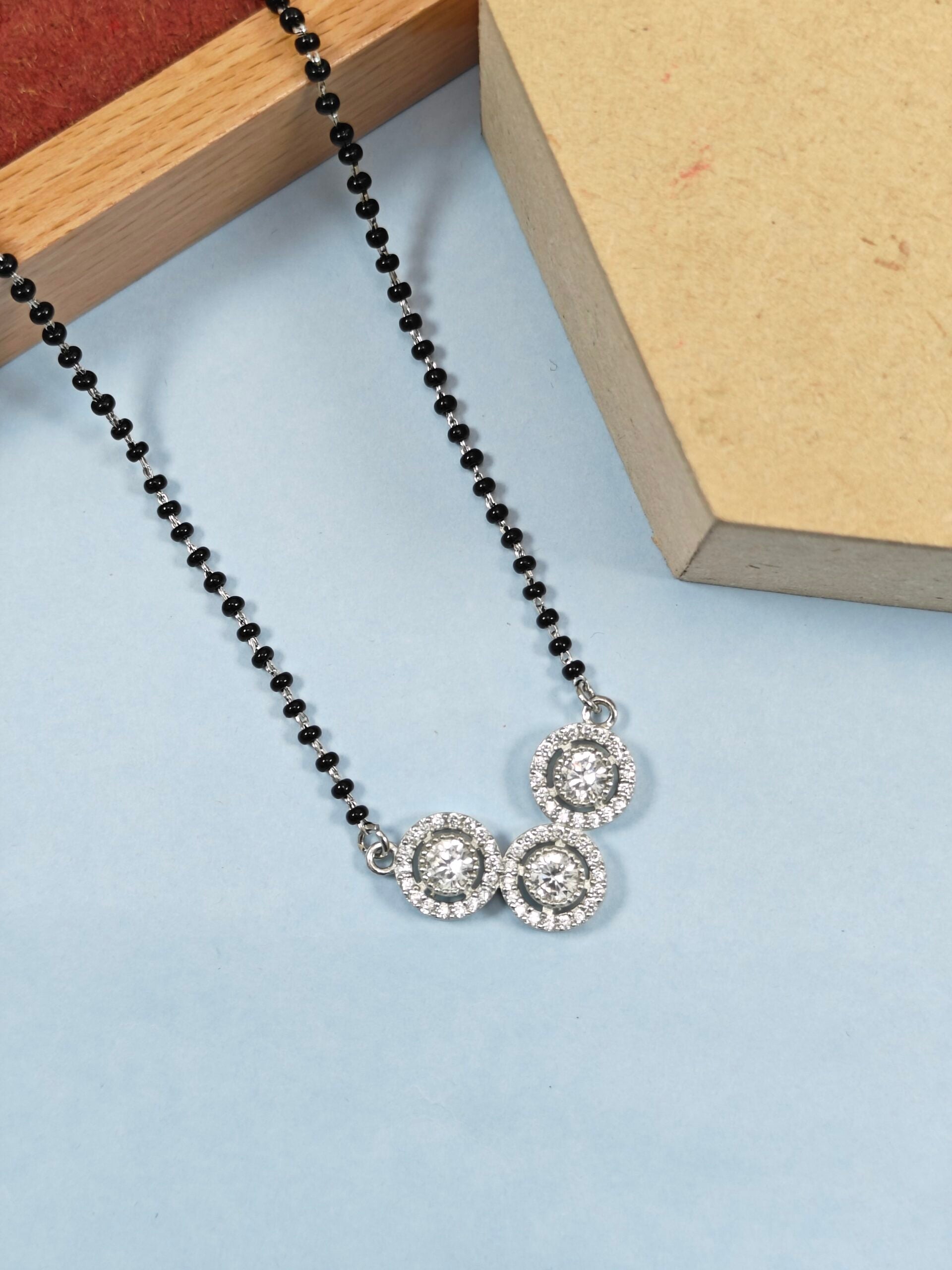 Necklace with black beads and silver pendants on a light blue surface