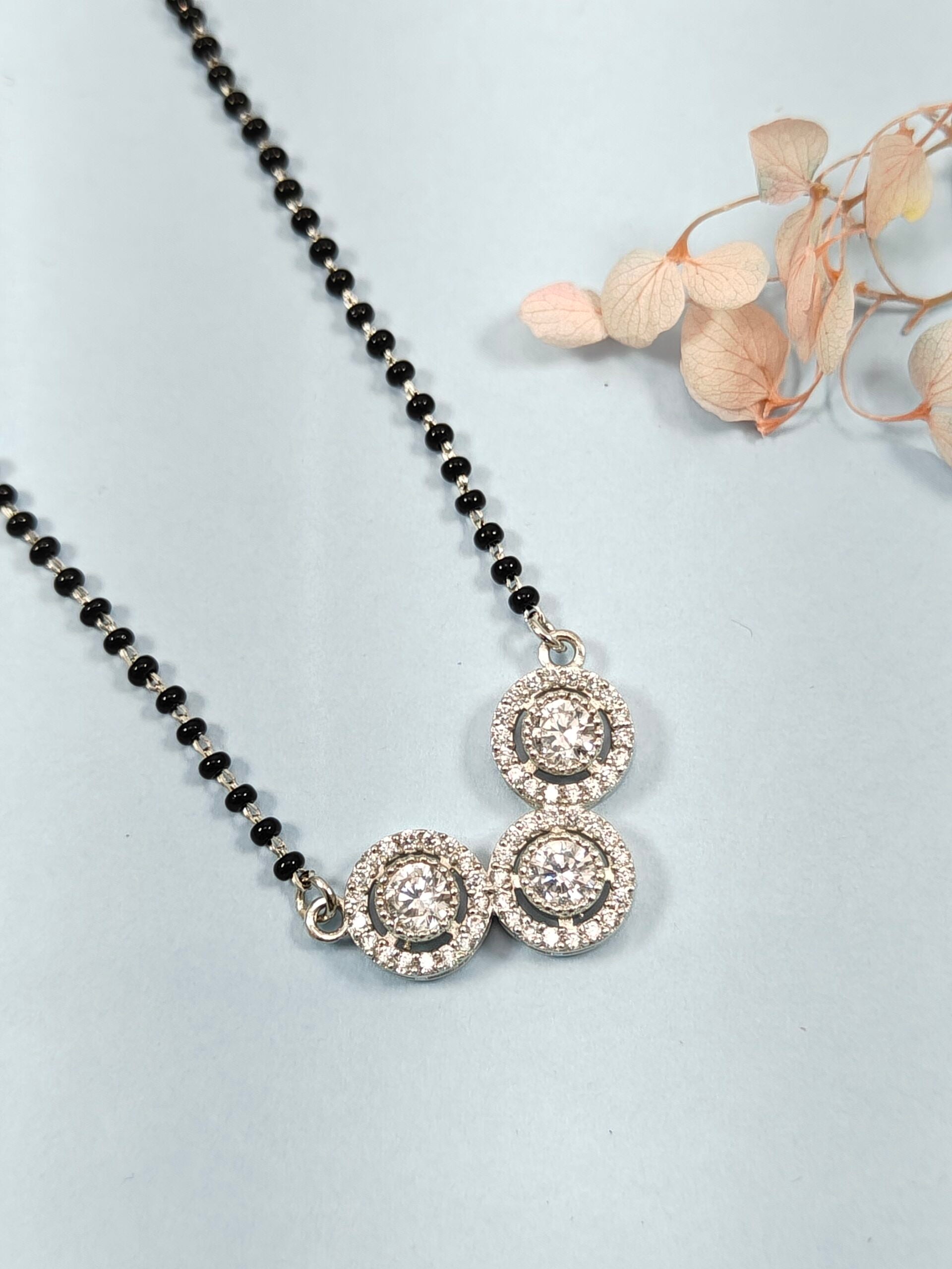 Necklace with black beads and silver pendants on a light gray background