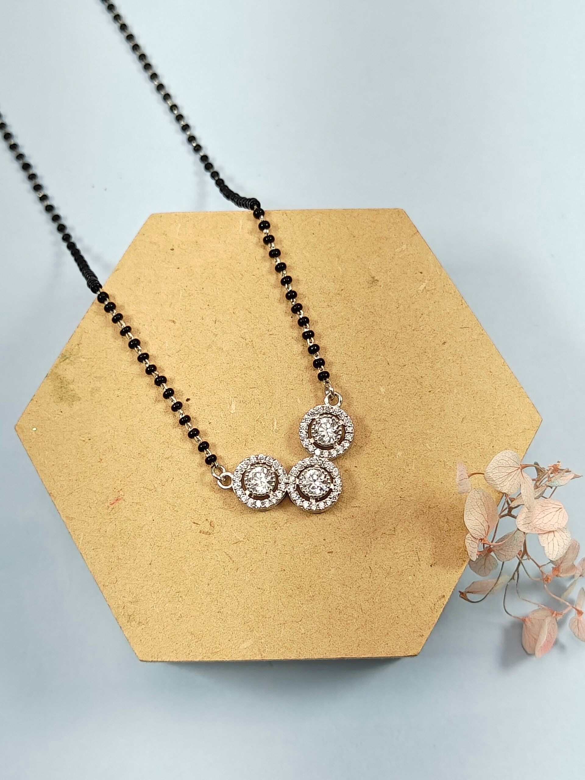 Necklace with black beads and silver pendants on a hexagonal wooden stand with dried flowers.