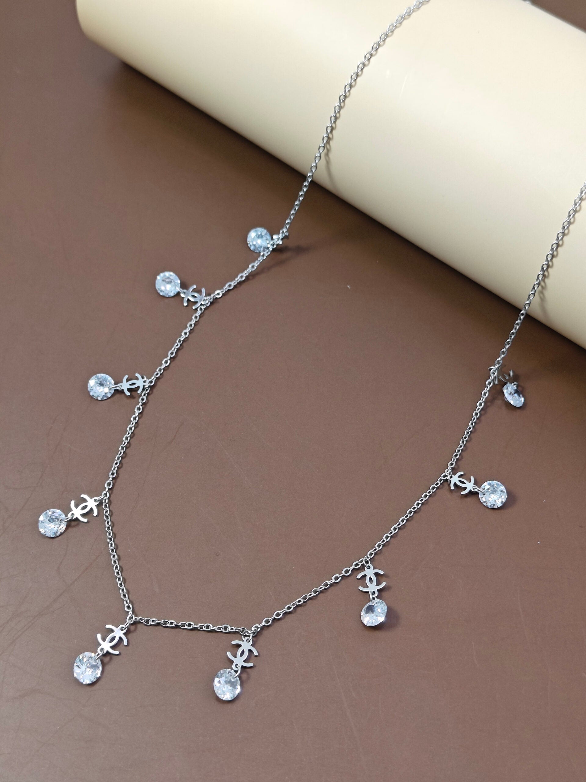 Silver necklace with crystal-like pendants on a brown surface