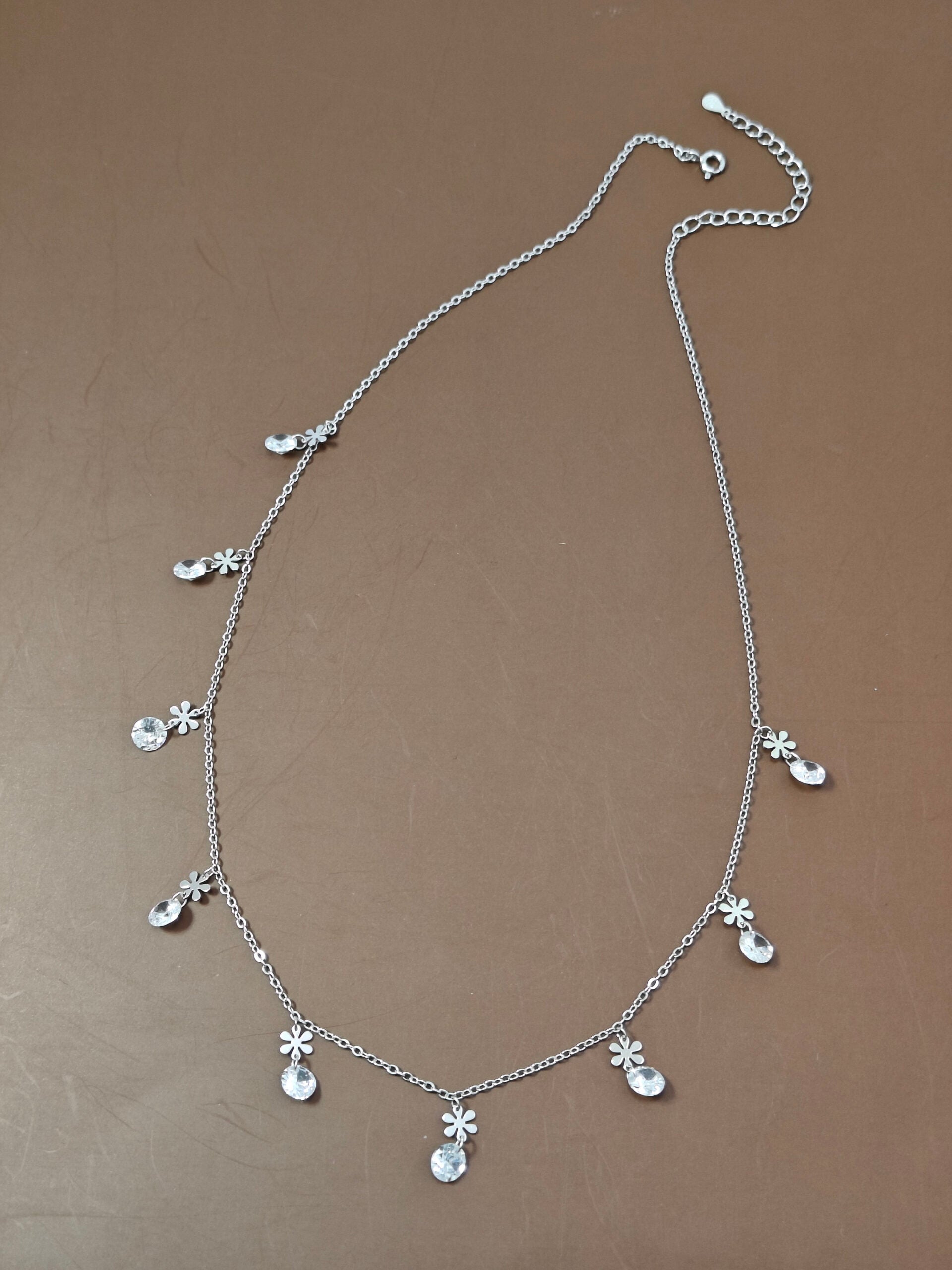 Silver necklace with floral pendants on a brown background