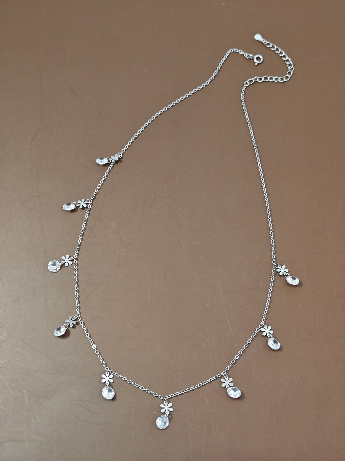 Silver necklace with floral pendants on a brown background