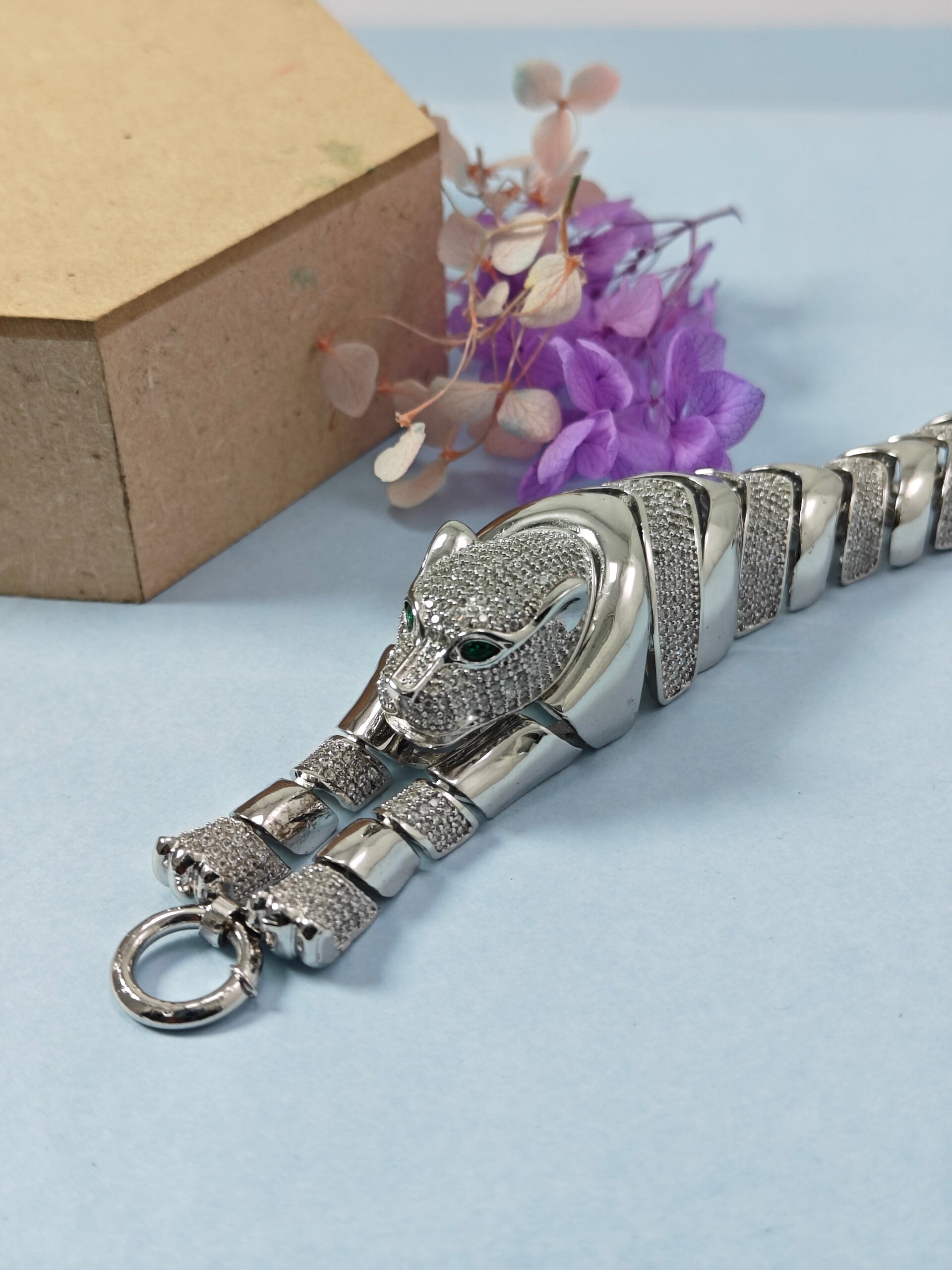 Silver panther keychain on a light blue surface with a cardboard box and flowers in the background