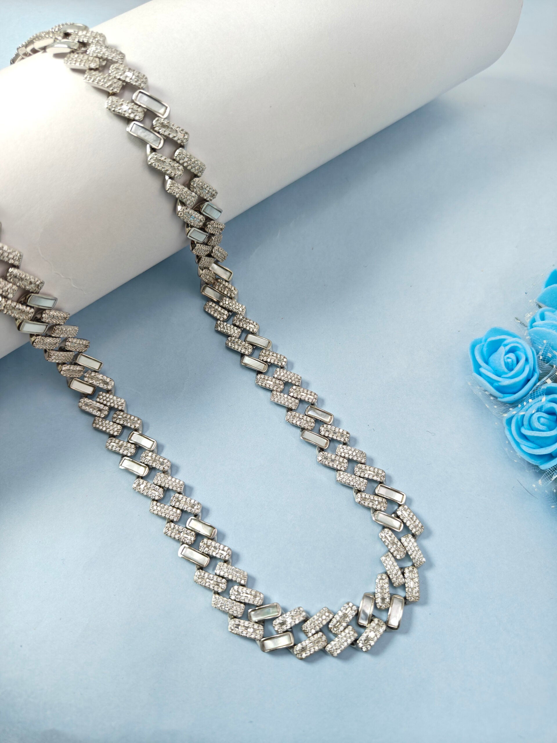 Silver chain necklace on a white mannequin with blue flowers in the background