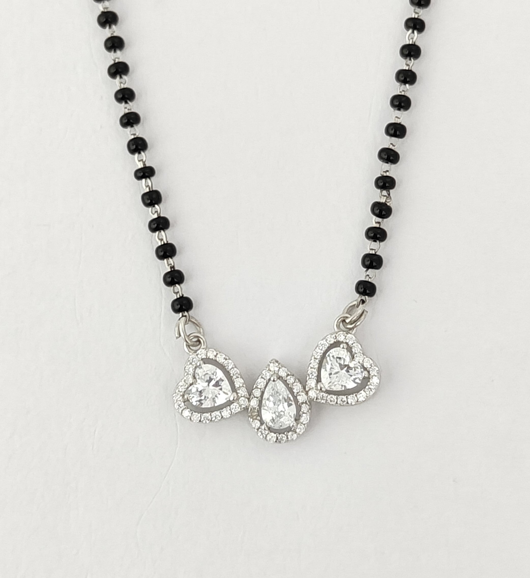 Necklace with black beads and heart-shaped silver pendants on a light gray background