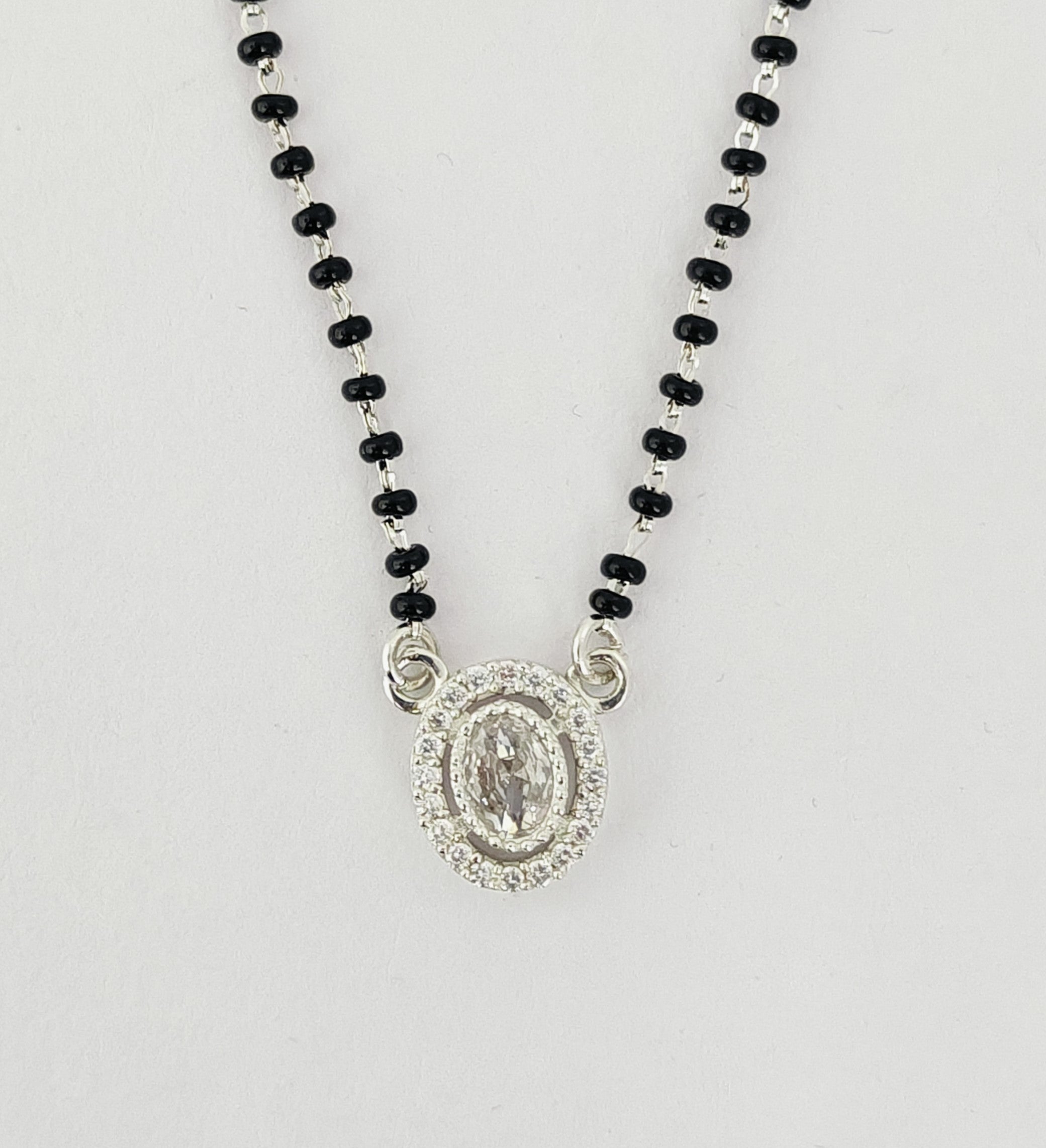 Necklace with black beads and a silver pendant on a light gray background