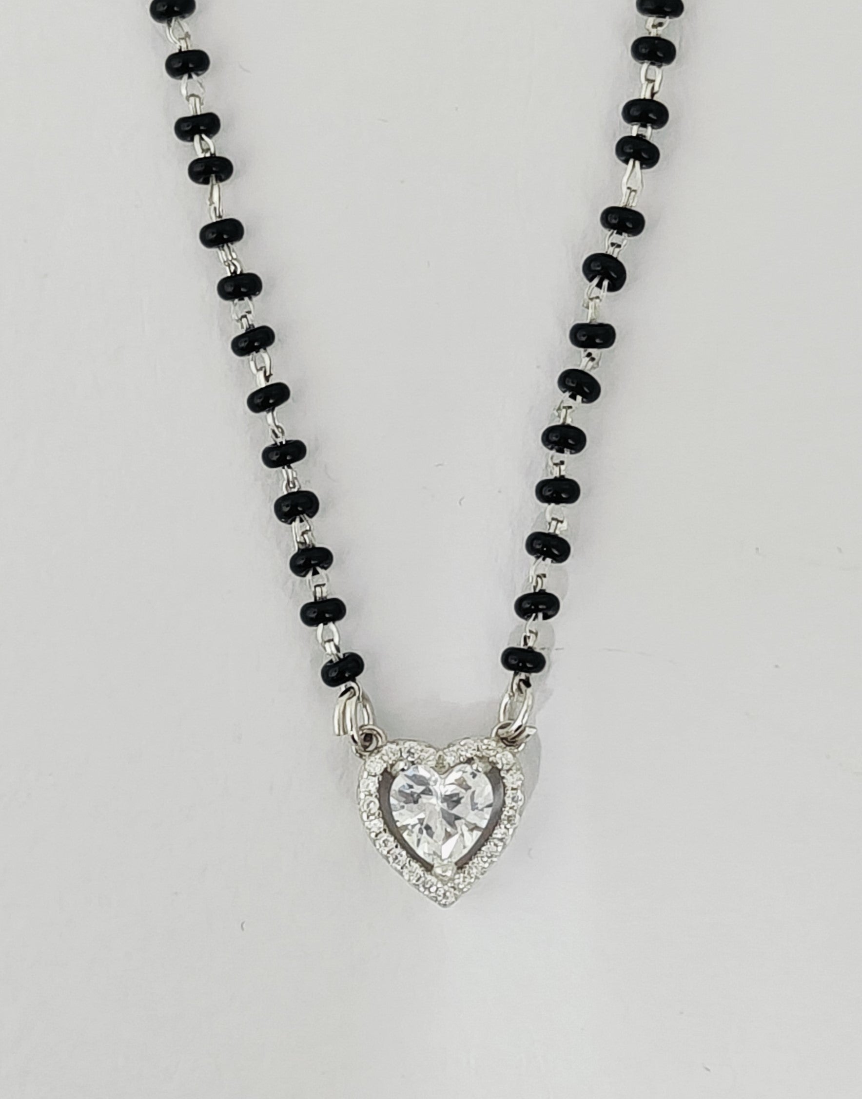 Necklace with heart-shaped pendant and black beads on a light gray background