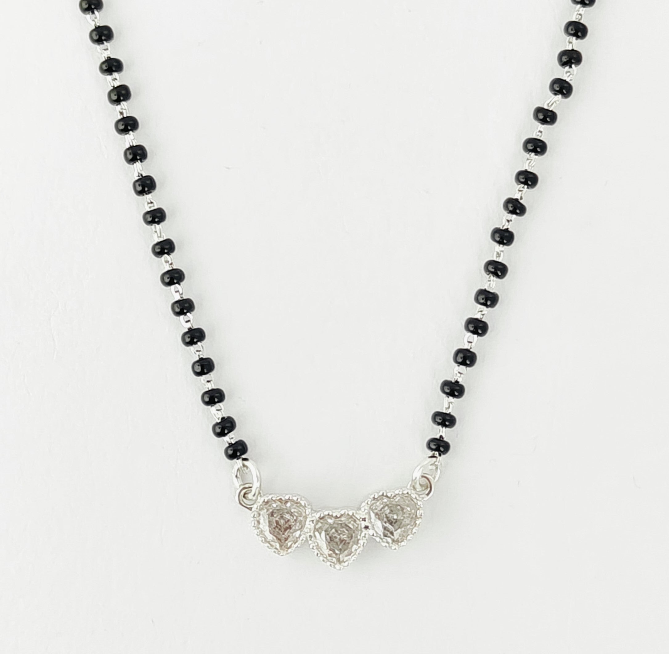 Necklace with black beads and silver heart-shaped pendants on a white background