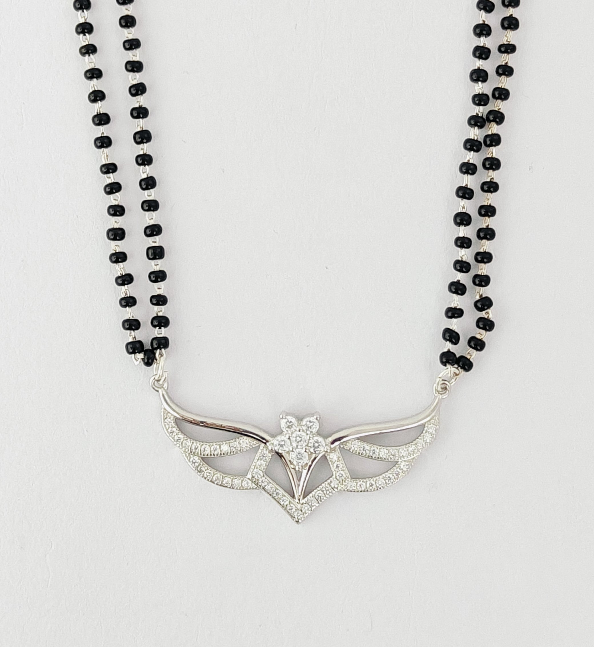 Necklace with black beads and a silver pendant on a light gray background