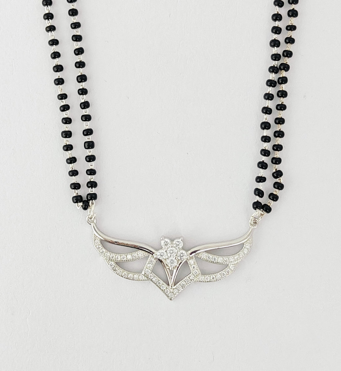Necklace with black beads and a silver pendant on a light gray background