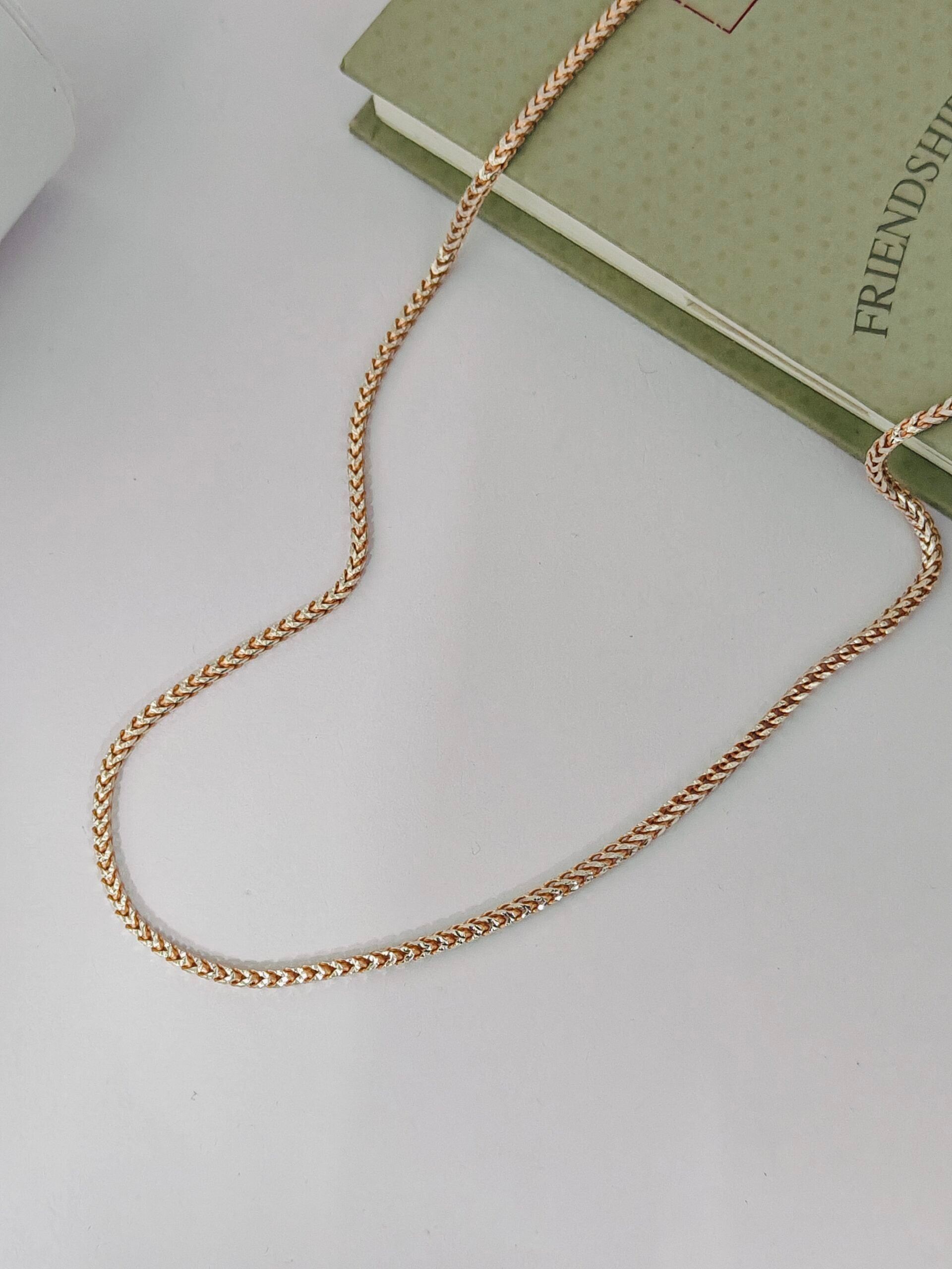 Gold chain necklace on a light gray surface with a green book in the background.