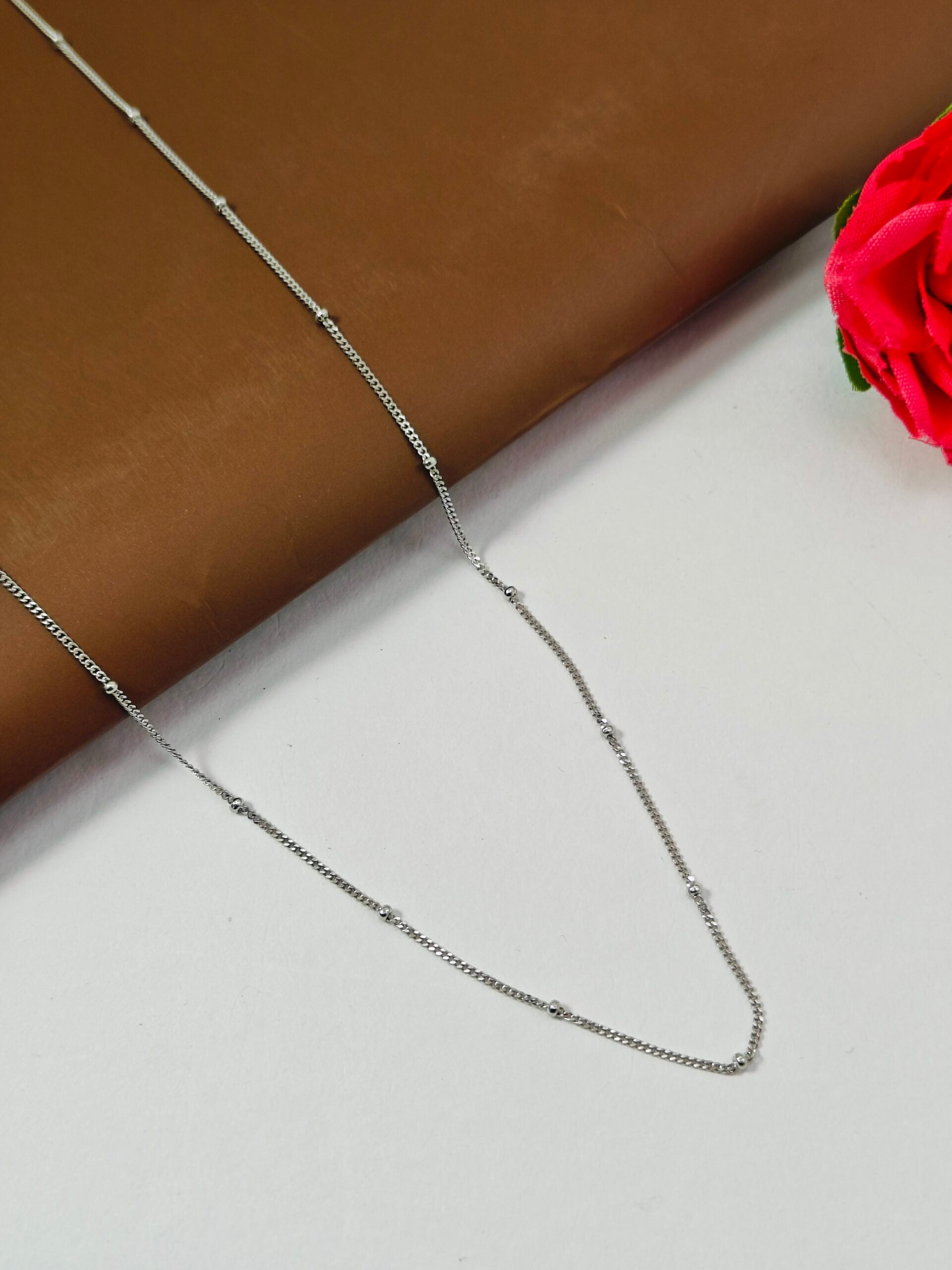 Silver chain necklace on a white surface with a brown fabric background