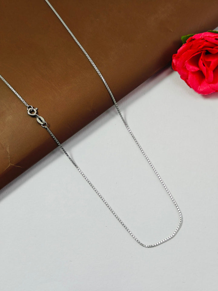Silver chain necklace on a white surface with a red flower in the background