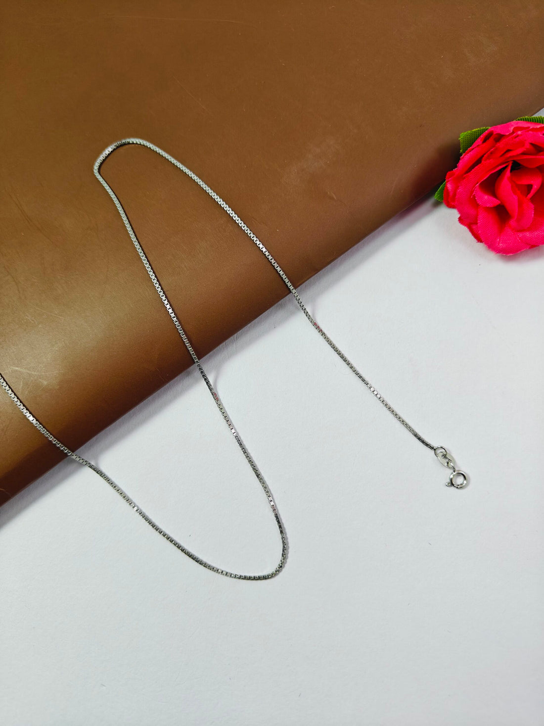 Silver necklace on a white surface with a pink flower in the corner